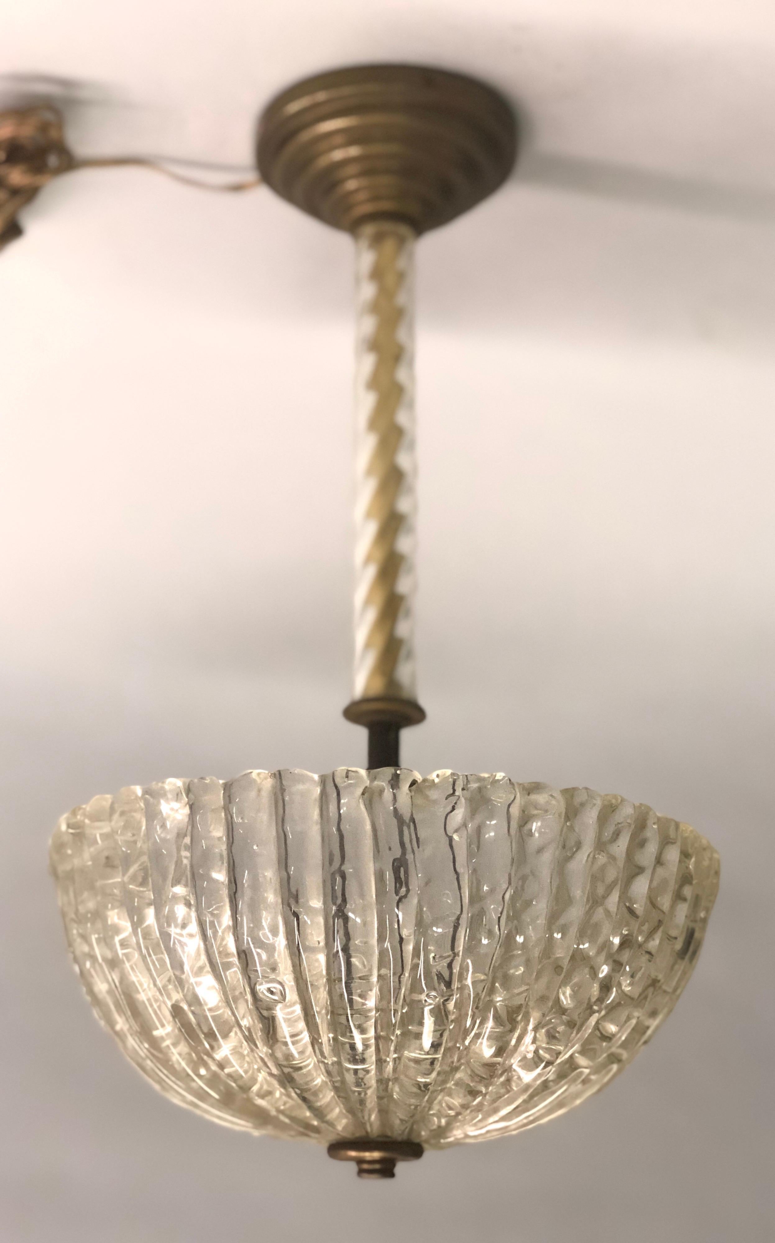 2 Italian midcentury hand blown Venetian glass chandeliers in the modern neoclassical spirit with hand blown shades by Barovier & Toso. The stems composed of clear twisted glass sitting on stepped bronze bases and with clear thick hand blown shades