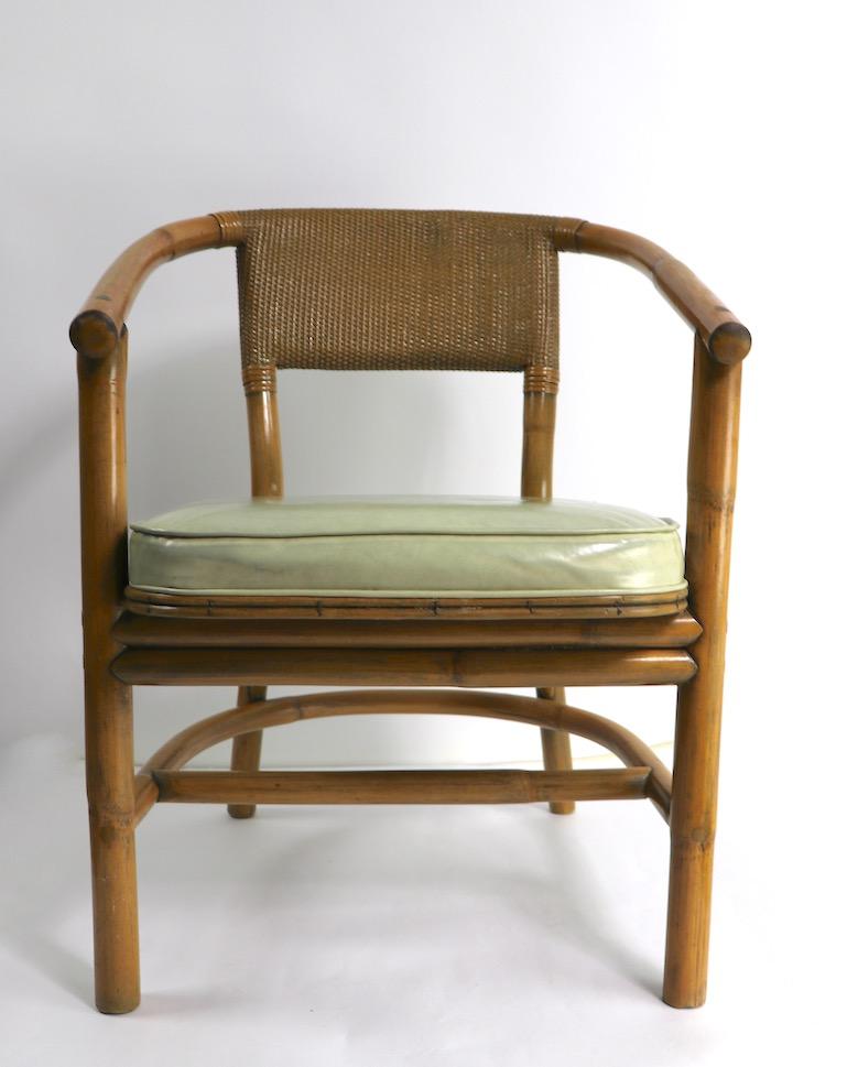 Stylish bamboo arm, lounge chairs, attributed to McGuire. Bamboo frames, with vinyl upholstered seats, and caned backrests. Both are in very good original condition, showing only light cosmetic wear, normal and consistent with age. Total H 30 x arm