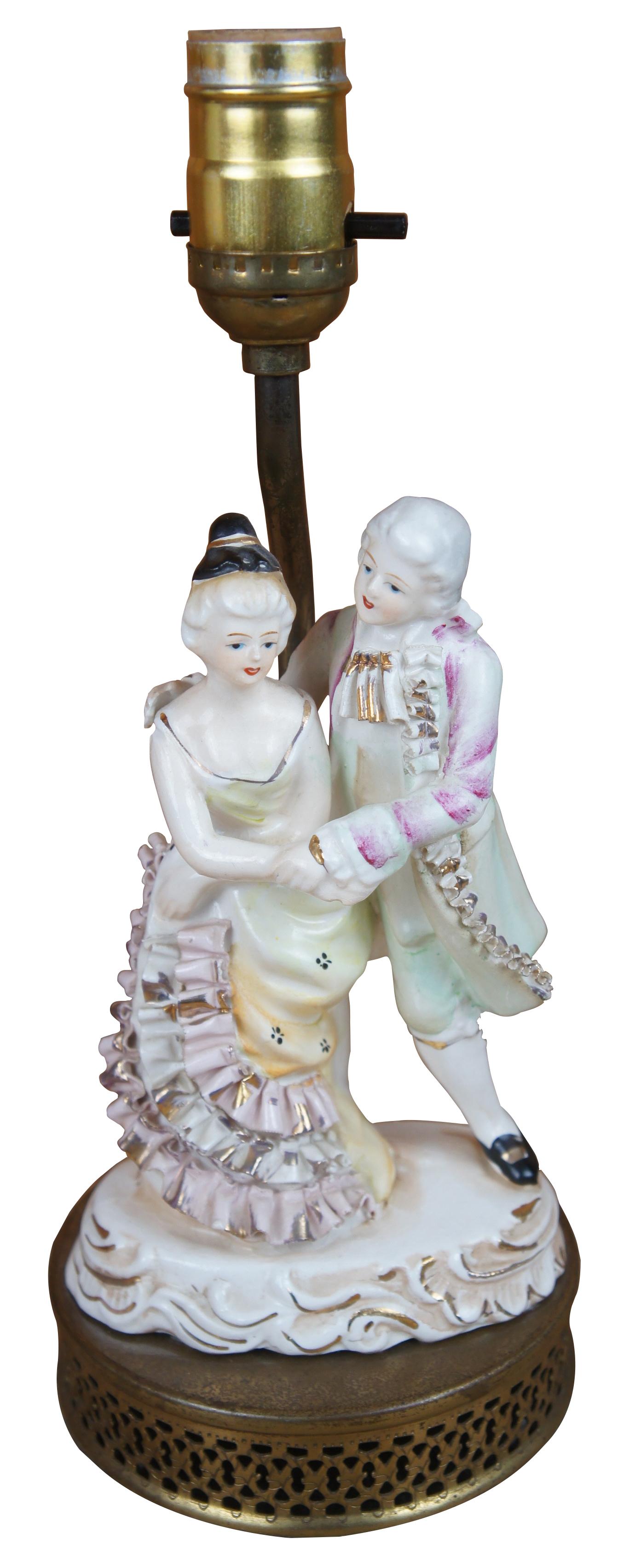 2 Mid-century reticulated brass and figural porcelain lamps featuring a pair of couples dressed in baroque or colonial attire dancing the waltz under cream shades.

Measures: 10
