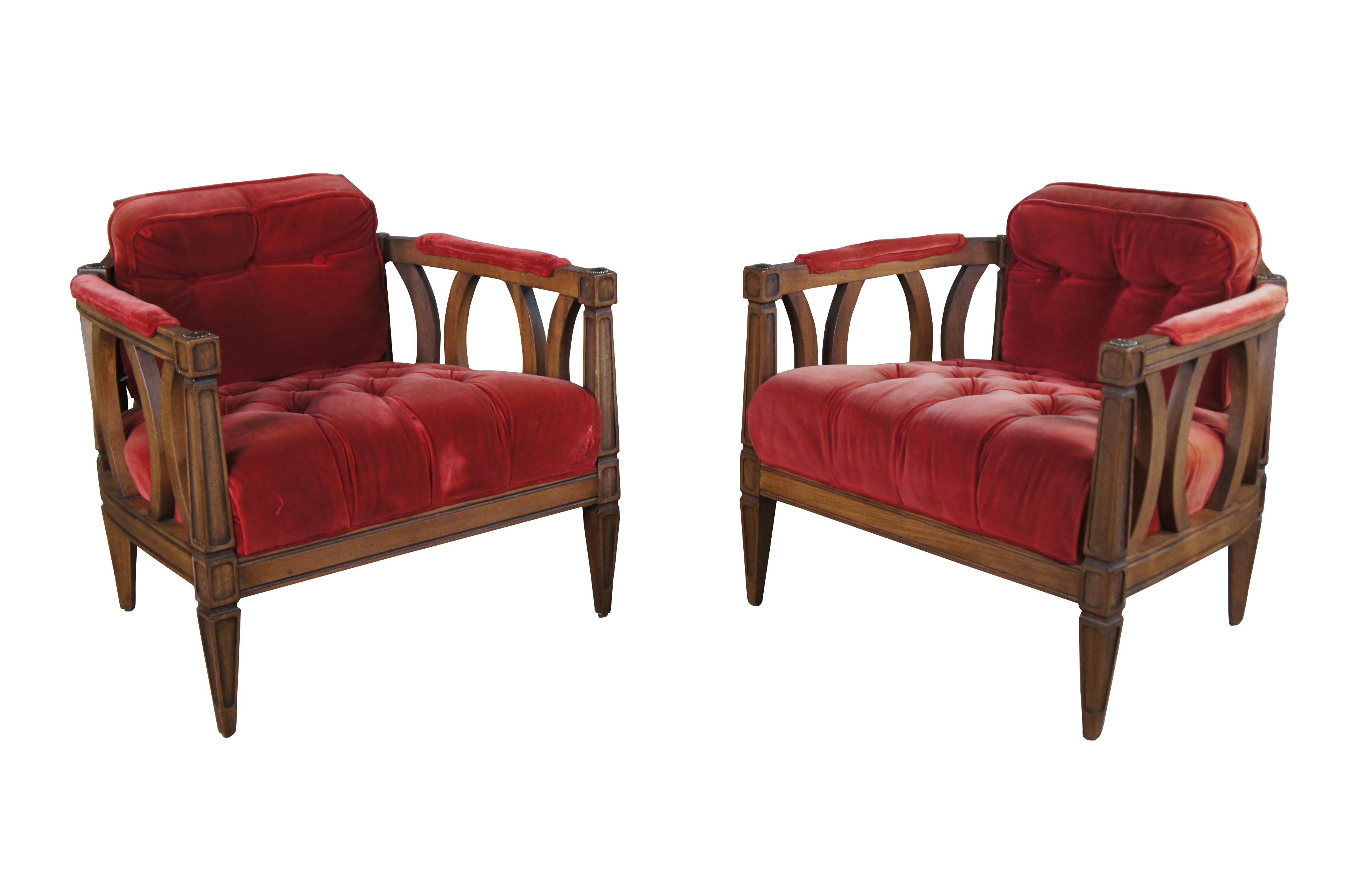 A pair of midcentury barrel back armchairs featuring a horse shoe shape with red velvet or velour tufted upholstery with high padded arms, and inset walnut panels with tapered legs.

.