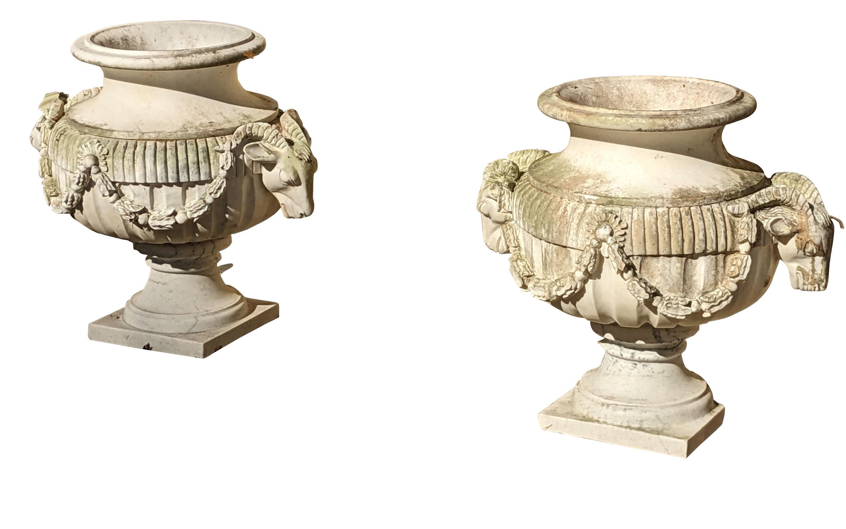 Stately pair or Figural Italian made Grecian style urn over stands.  Each is beautifully crafted from marble with Ram / Goat heads at each side.  Features a foliate drapery motif connecting each ram head and fluted / reeded exterior.  
