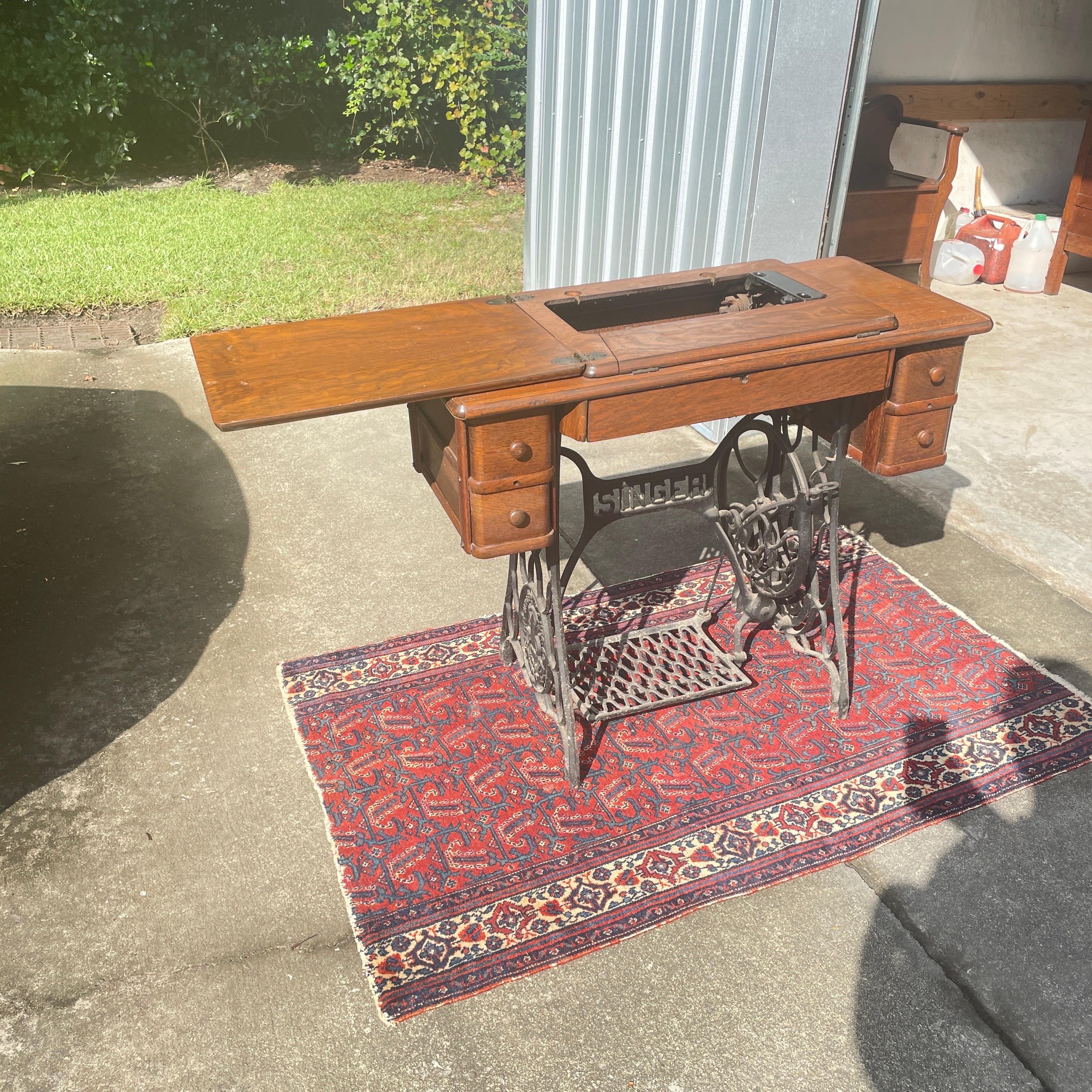 An antique oak sewing machine table with an iron base. As you can see in the first pictures it is of the table in the open position. The antique sewing machine was removed some time ago, but the table retains the original treadle and knobs. This