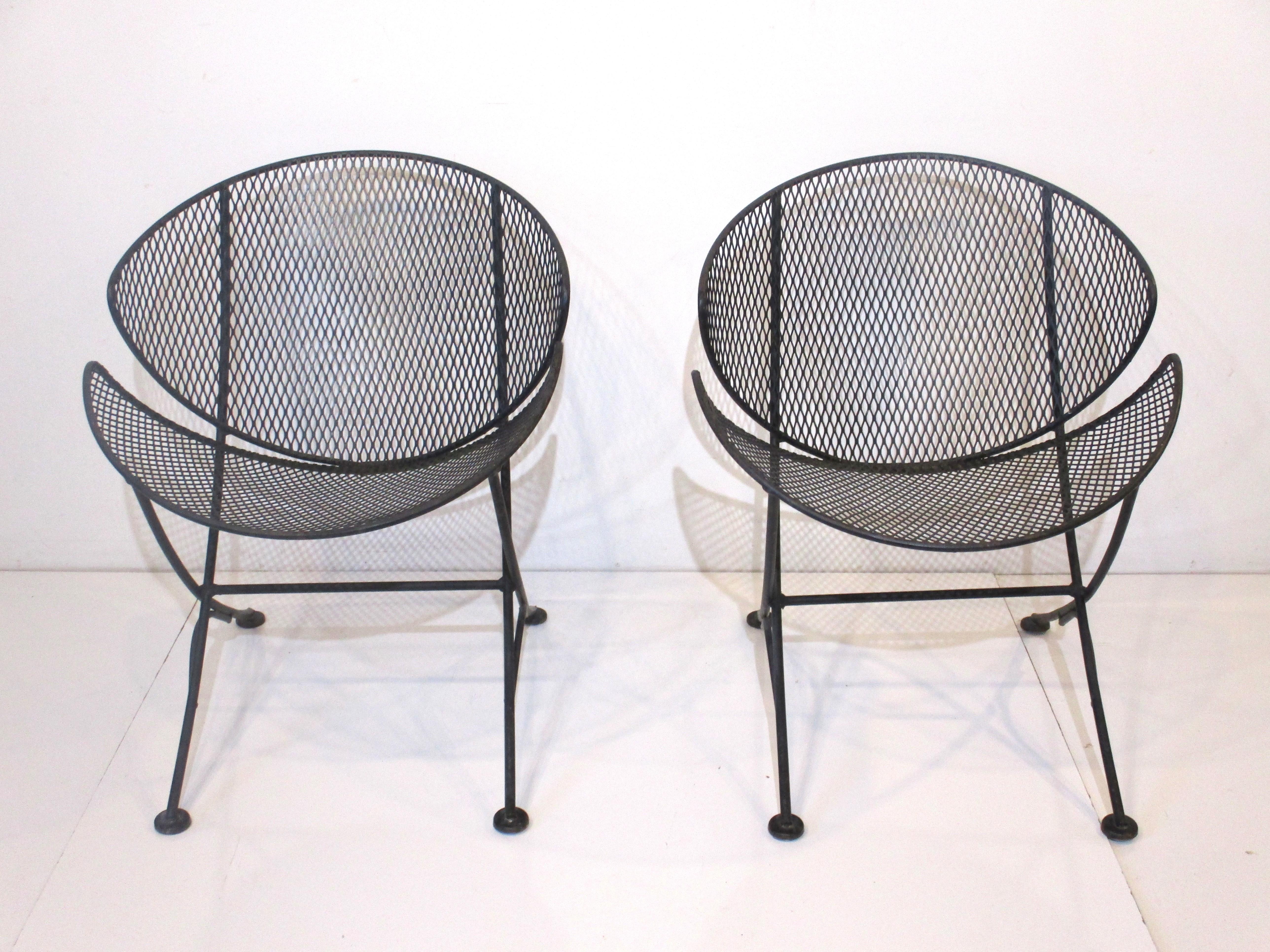 A pair of well crafted iron and mesh metal Orange Slice chairs in a flat black finish with contoured seat and back. The sculptural look and feel of these chairs will enhance any garden , deck or three seasons room and having flat foot pads makes
