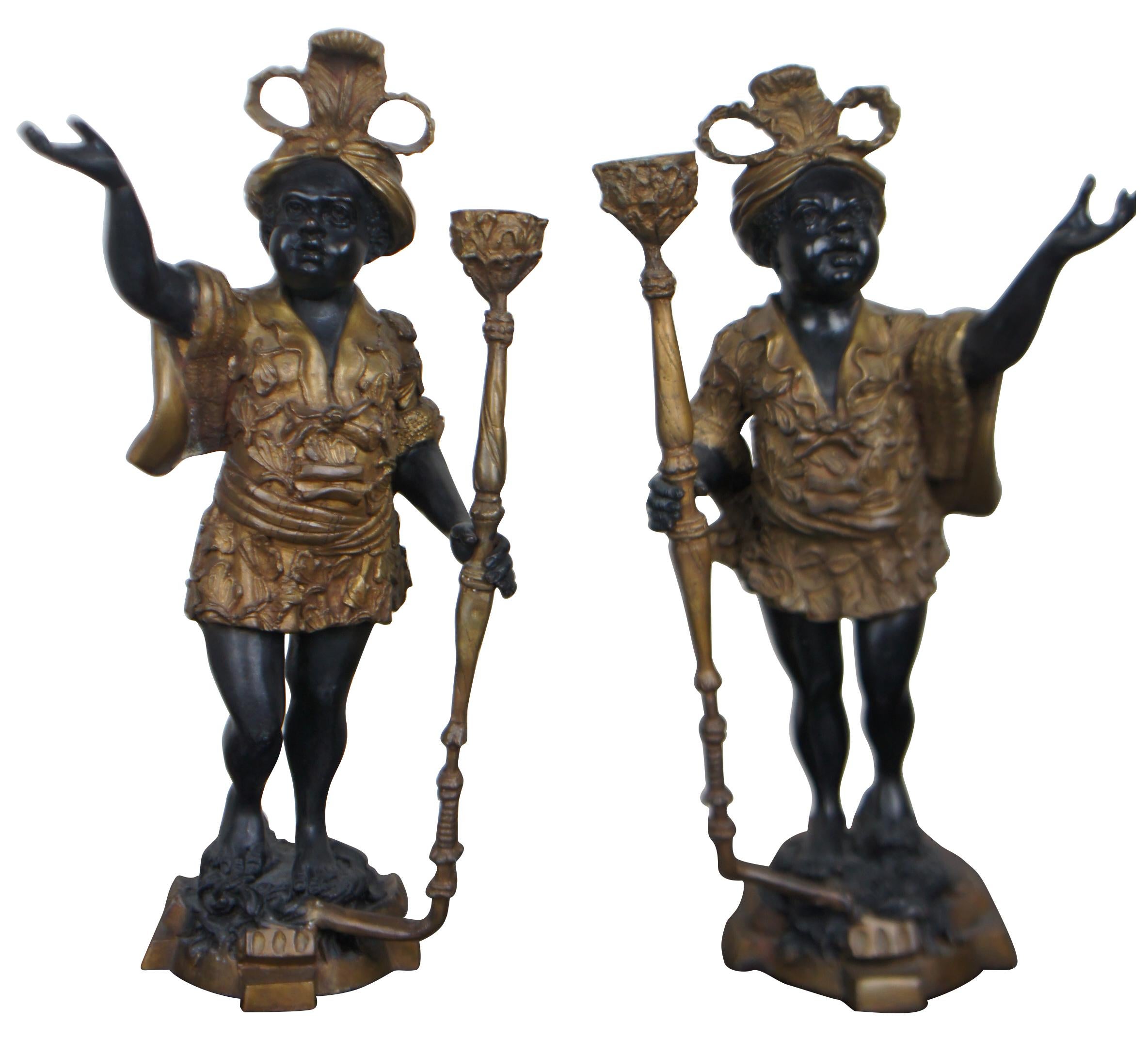 Pair of black and gold heavy cast bronze sculptures in the shape of boys in feathered turbans and baroque attire, holding candleholder staffs or torchieres (torch). Measures: 18