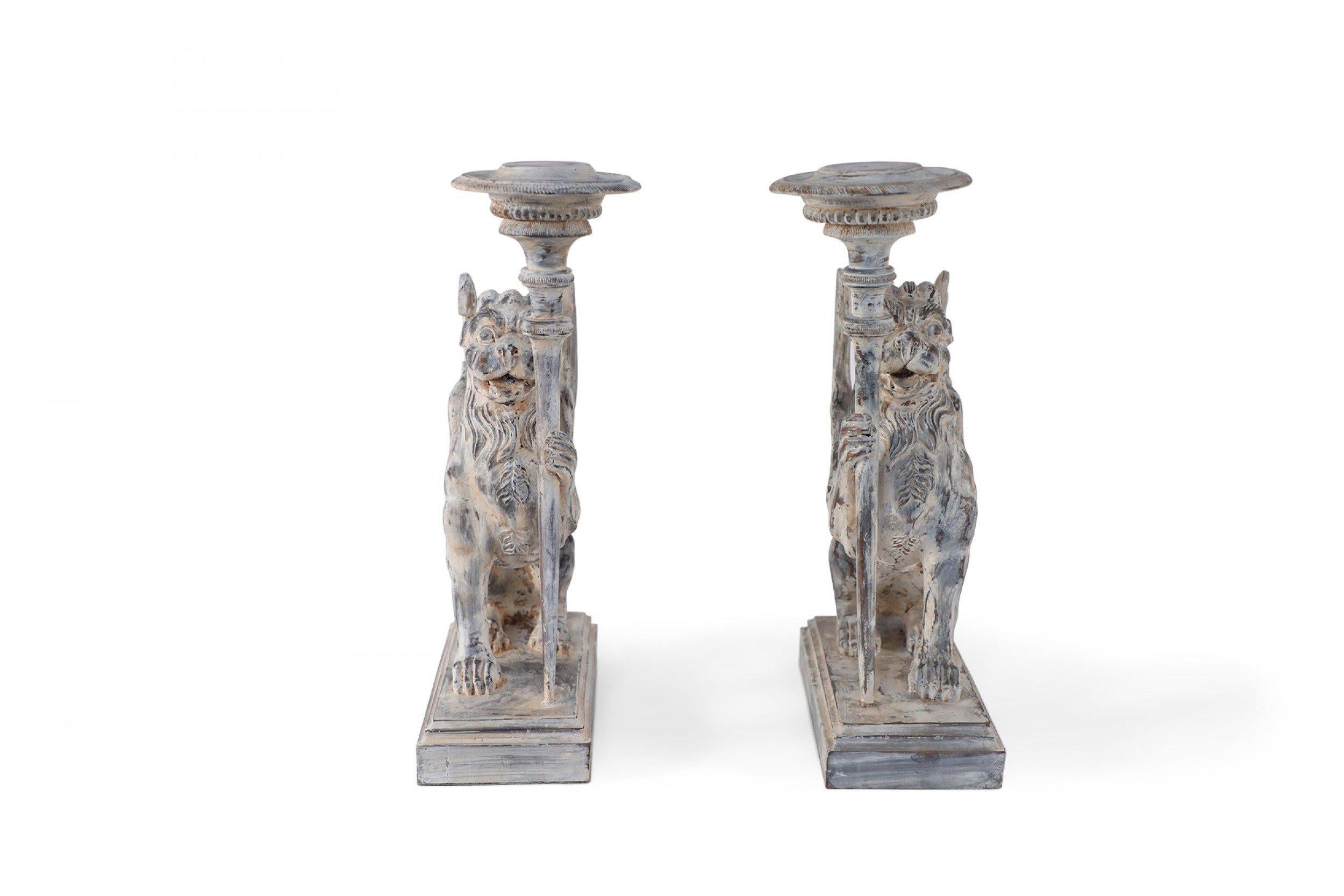 2 Paare von mythologischen geschnitzten Holzkerzenhaltern / Buchstützen in Form von Chimären, die einen Kerzenständer in einer Hand halten, auf gestuften rechteckigen Holzsockeln mit weißer Oberfläche. (PREIS PRO PAAR).
 