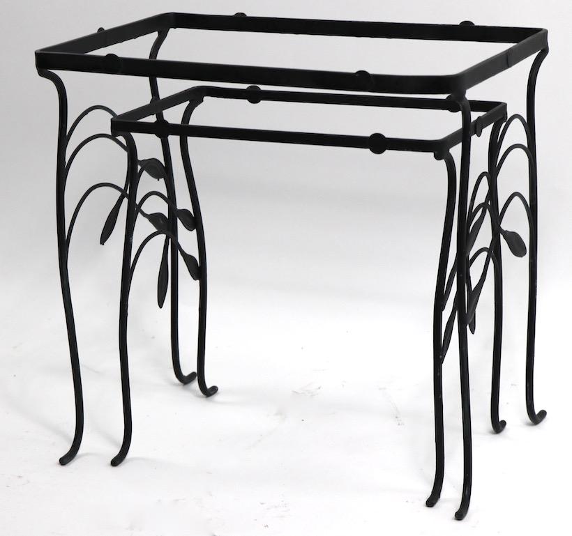 Stylish set of two nesting tables in wrought iron with foliate motif design. Tables originally had a glass tops offered and selling without glass. Dimensions of larger table: 20.25 W x 14 D x 19.5 H Smaller table 16 W x 10.25 D x 16.5 H. (inches).
