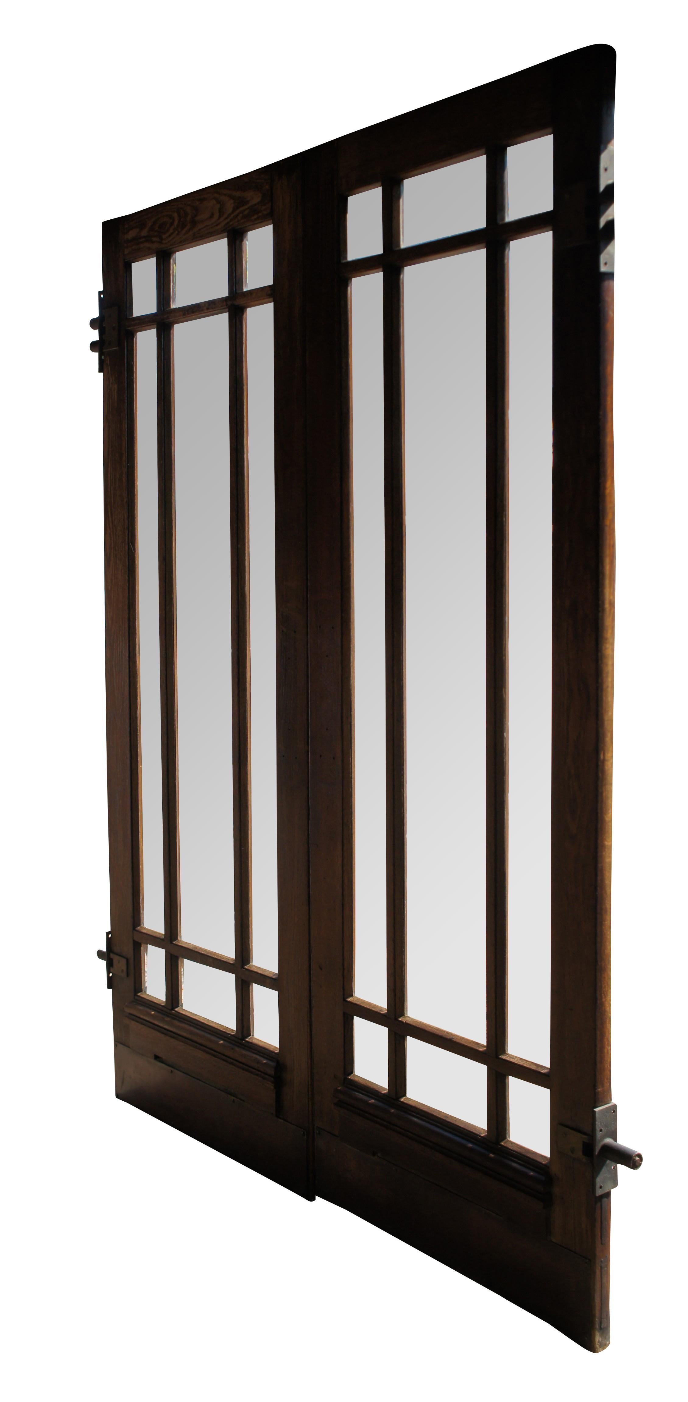 Pair of Mid Century French Saloon Swinging / Pivot Double Doors. Feature an oak frame with Prairie style lattice shaped center and beveled glass panels. The door is accented with brass mounted kickplates and Hawgood Systems Spring