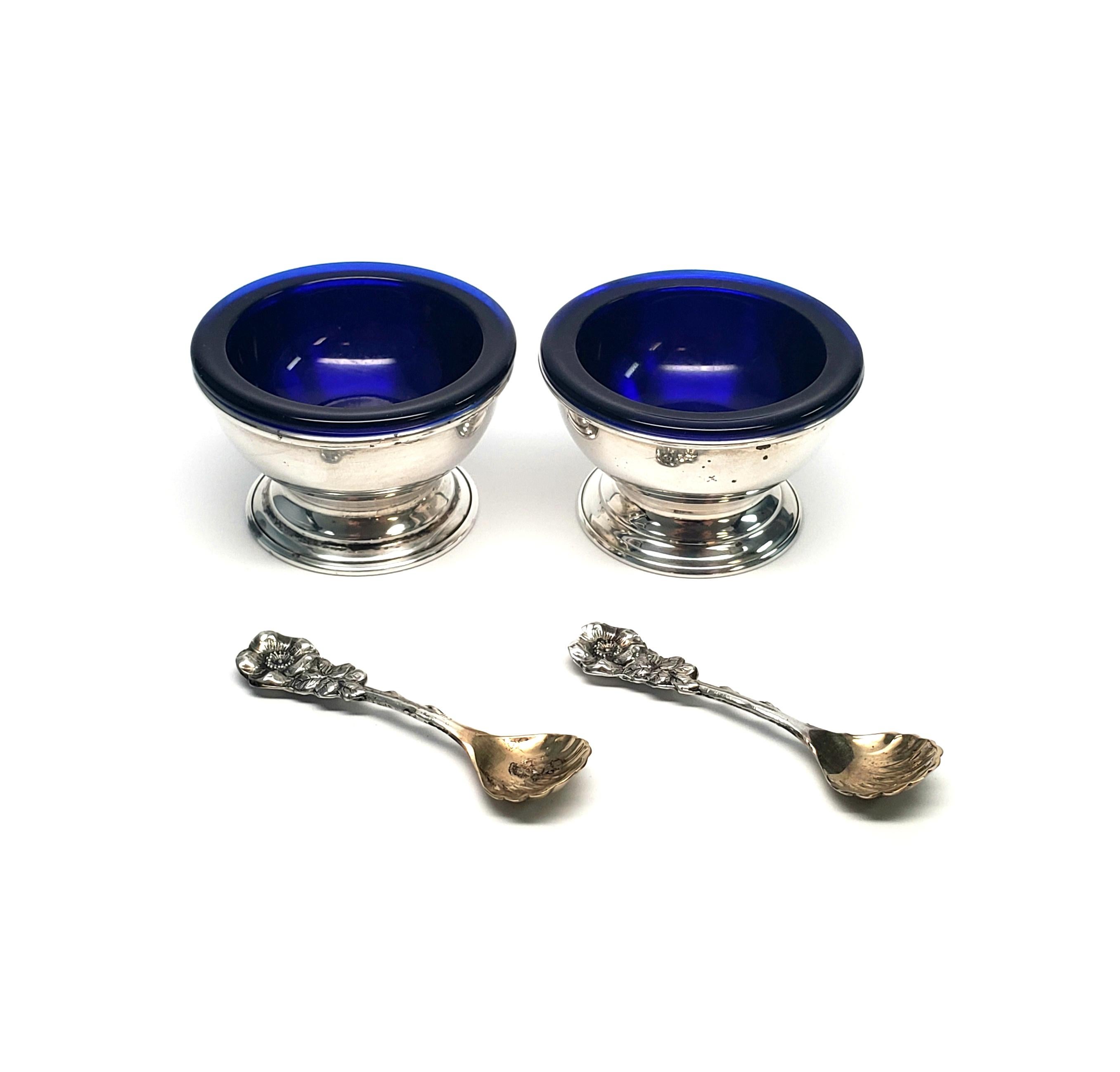 Boxed Set of 2 Reed & Barton salt cellars with 2 spoons.

Salt cellars each feature a removable cobalt blue glass bowl inside a sterling silver pedestal base. Set also includes 2 spoons with gold washed shell bowls and floral design