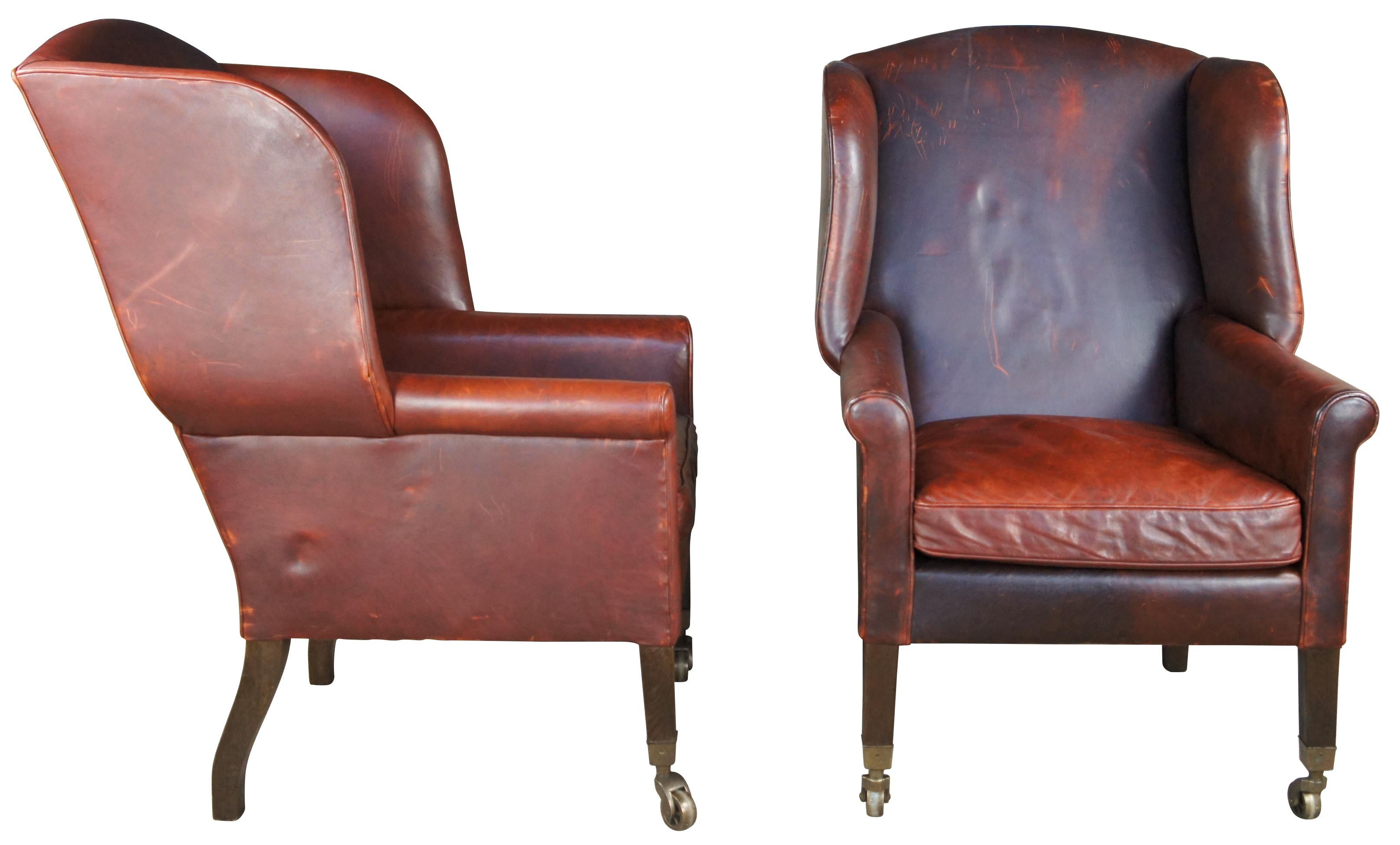 An English 1800s inspired brown leather fireside chair from circa. Features an arched top and deep, sheltering wings down to the swiveling, spoked brass casters, engraved with S Dobbins & Co Patent, Bristol. With low, padded scroll arms and a plump