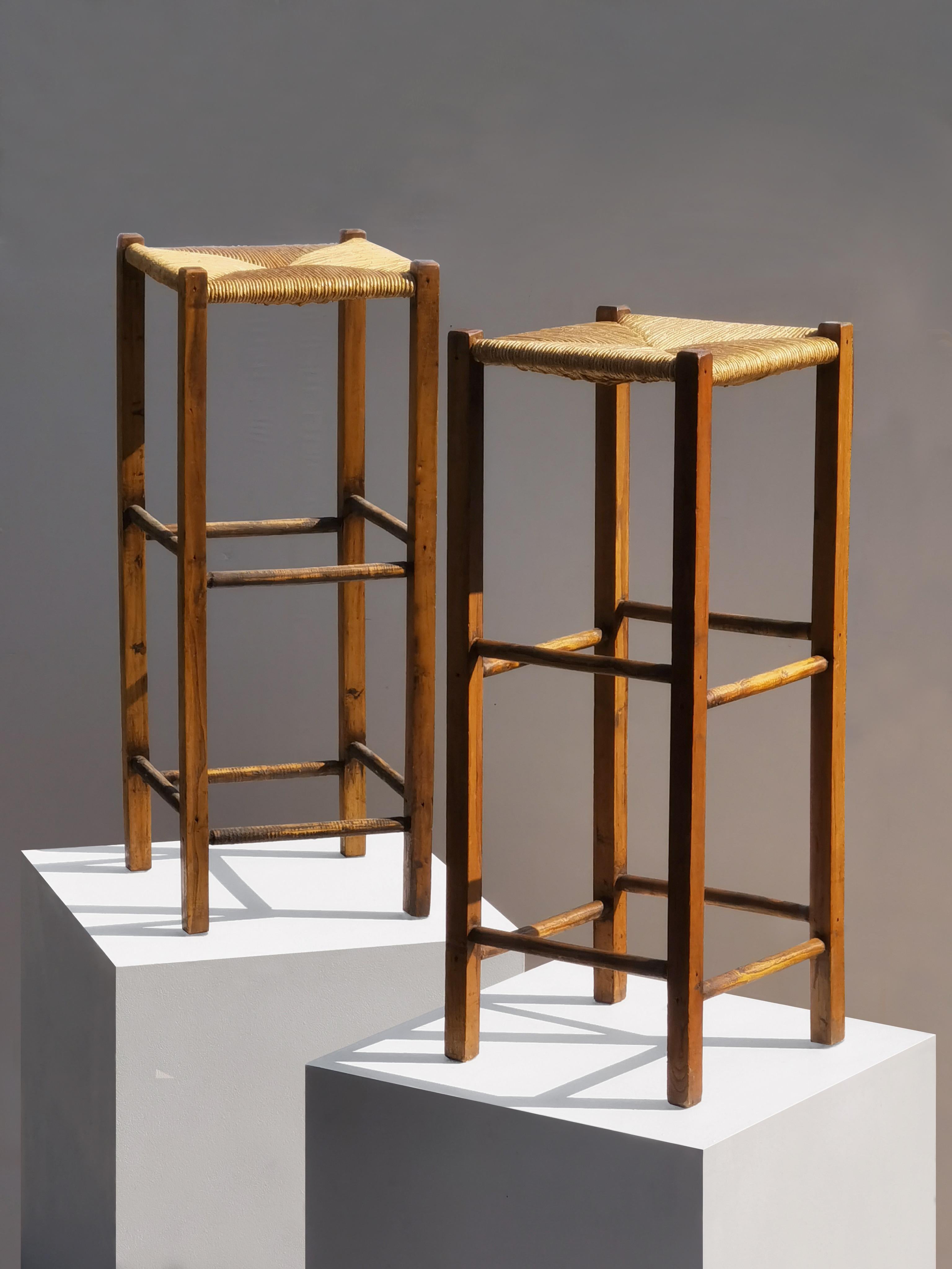 A pair of thin and architectural high bar stools, Mid-Century Modern, Modernist, Rustic Modern, Brutalist, square and thin oak structures, square and comfortable straw seating areas, the spirit of the creations of Charlotte Perriand, by french