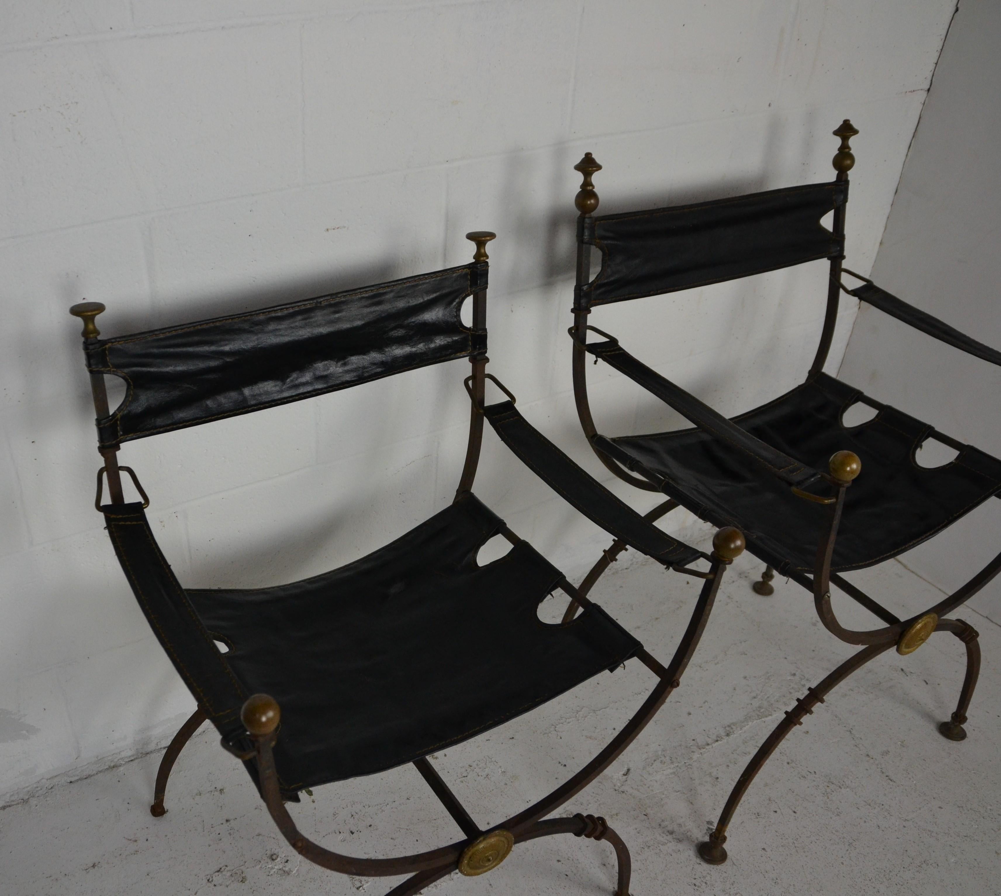 2 1920s Savonarola iron and brass chairs. Iron frames with brass finials. Brass medallion to the front of the X-stretchers. Upper finials miss-matched and pad feet missing on slightly lower chair. So sold As-Is.