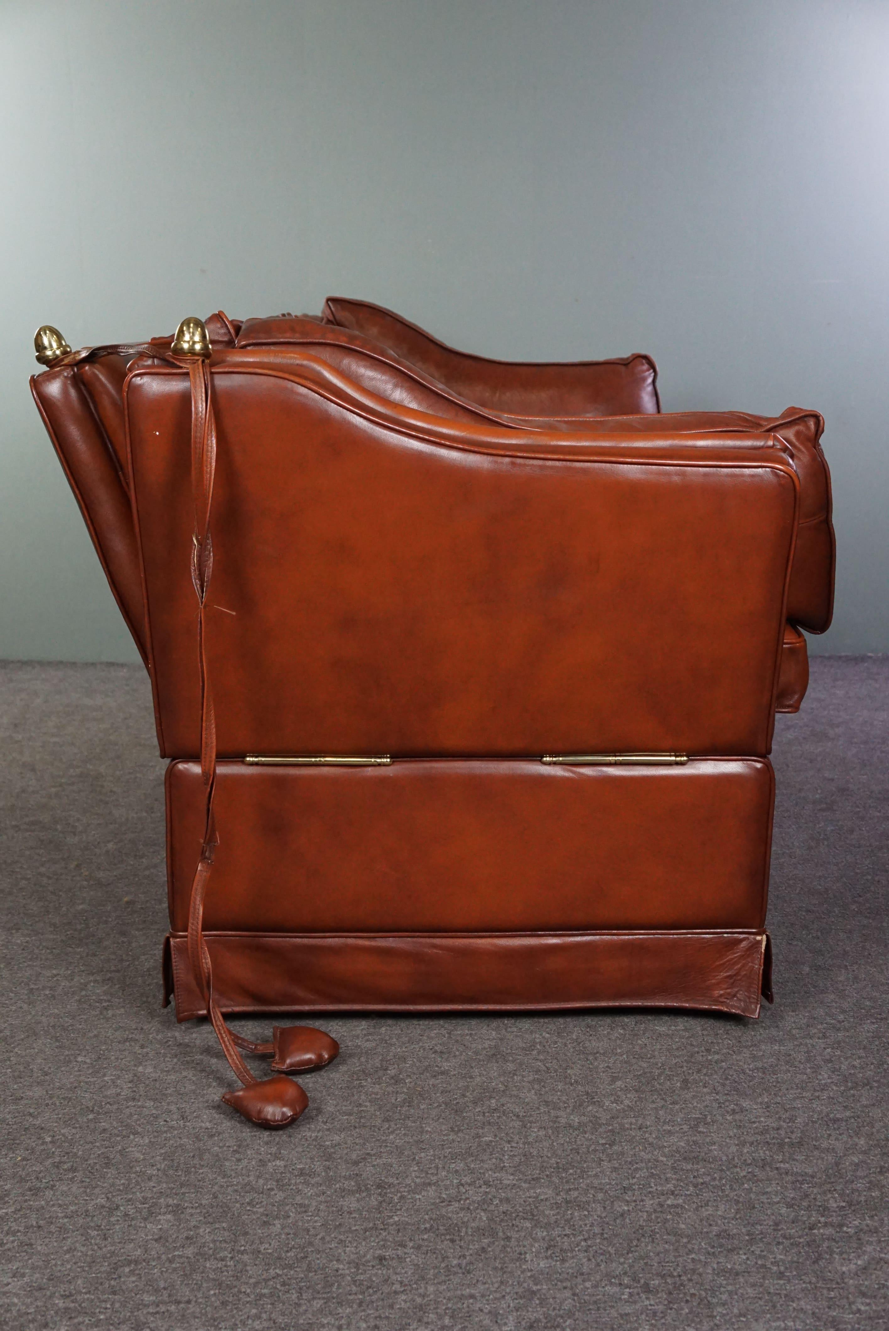 Offered is this beautiful cognac-colored cowhide leather 2-seater castle bench with gold-colored details. Castle benches not only boast their name for grandeur but also for their appearance. With their foldable armrests and stately presence, they