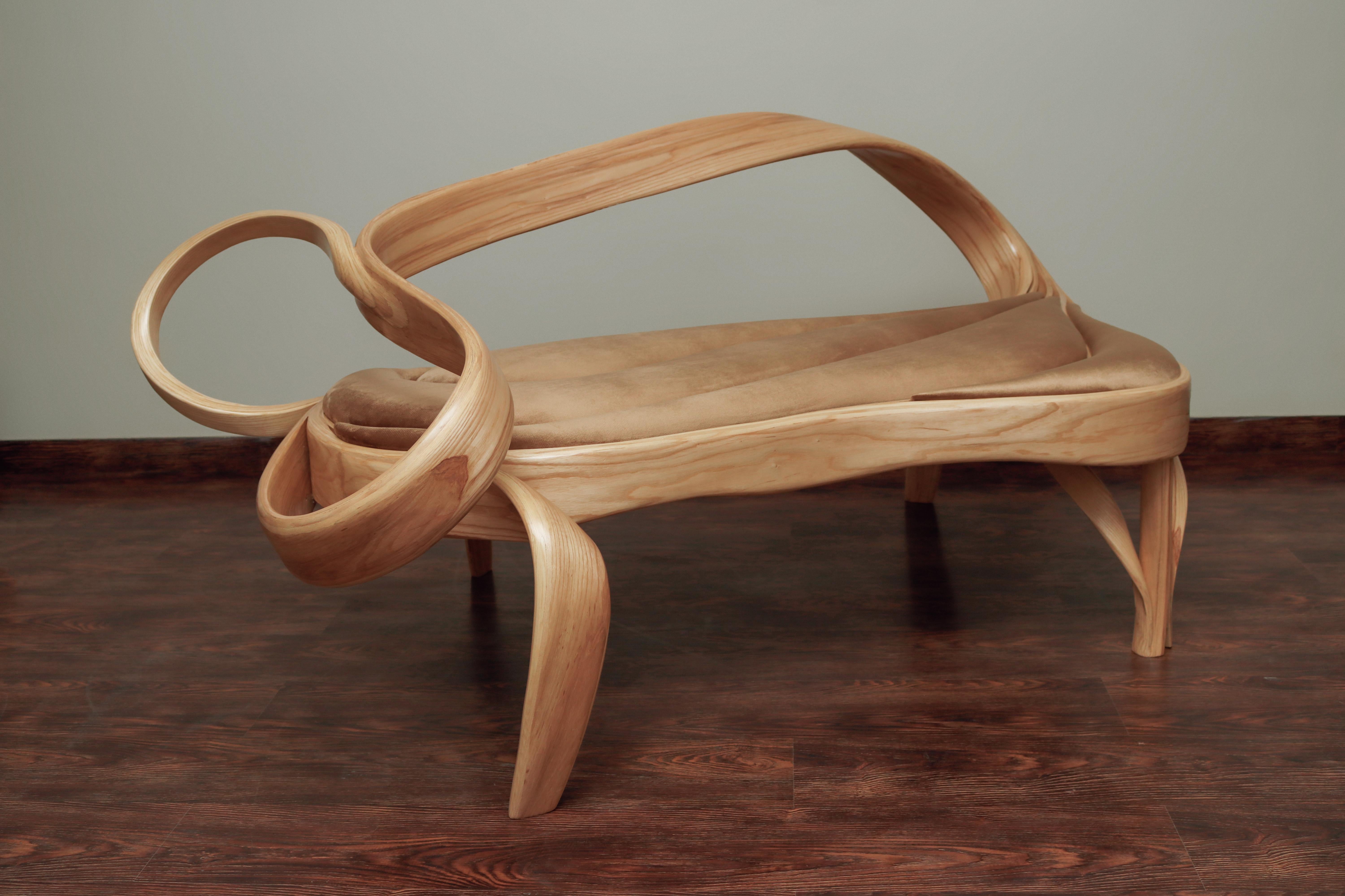 This piece features a unique design element where the main frame and the inner layers of wood converge to create the back-rest of the piece in a natural flow. The legs of the sofa seamlessly emerge from the frame. All these elements combined create