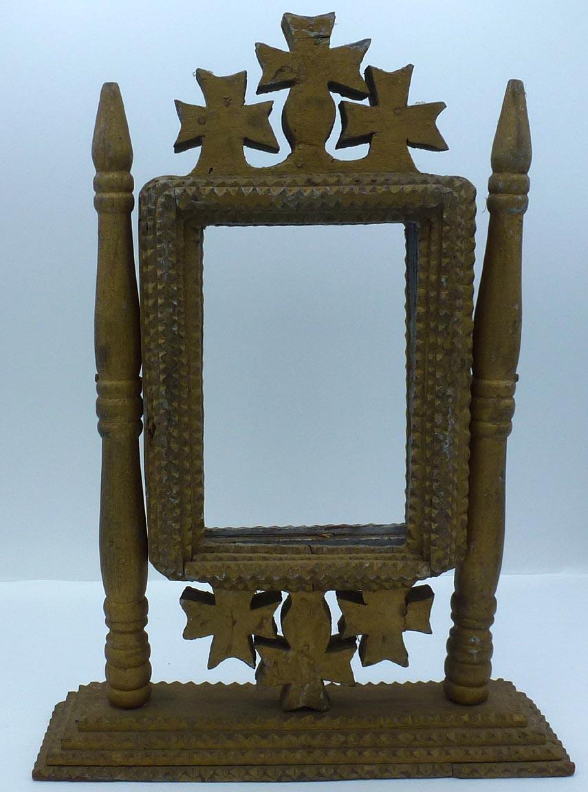 This is a 2-sided, free-standing tramp art frame. It has two turned uprights which are pegged into the four-layer, chip carved base. The frame itself swivels between the uprights. It has three crosses at the top and bottom, with four layers of chip