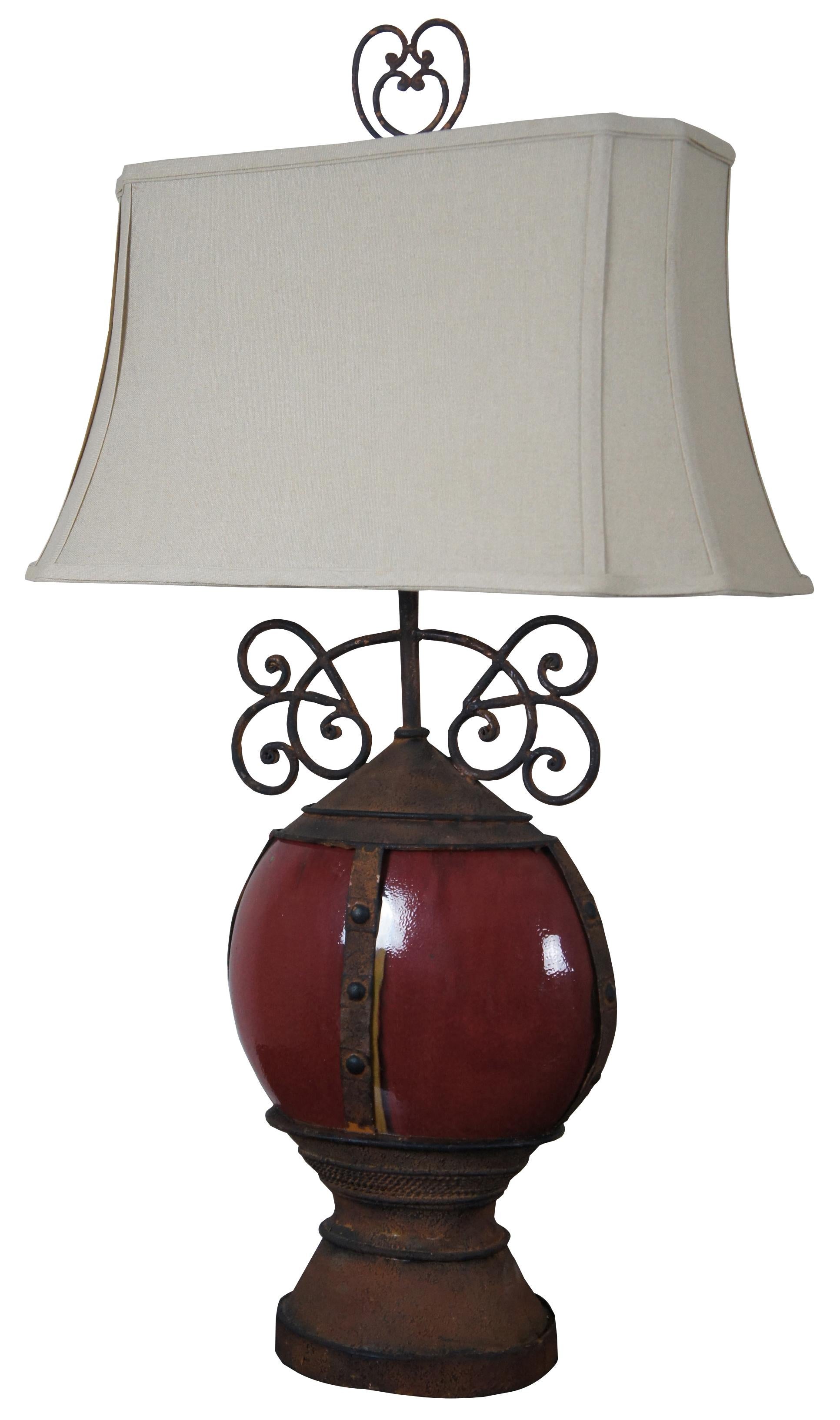 Pair of rustic round oxblood ceramic table lamps with iron bands, bases and scrolled accents.

Measures: Shade 20.5” x 10” x 10.75”, height to top of finial 34”.