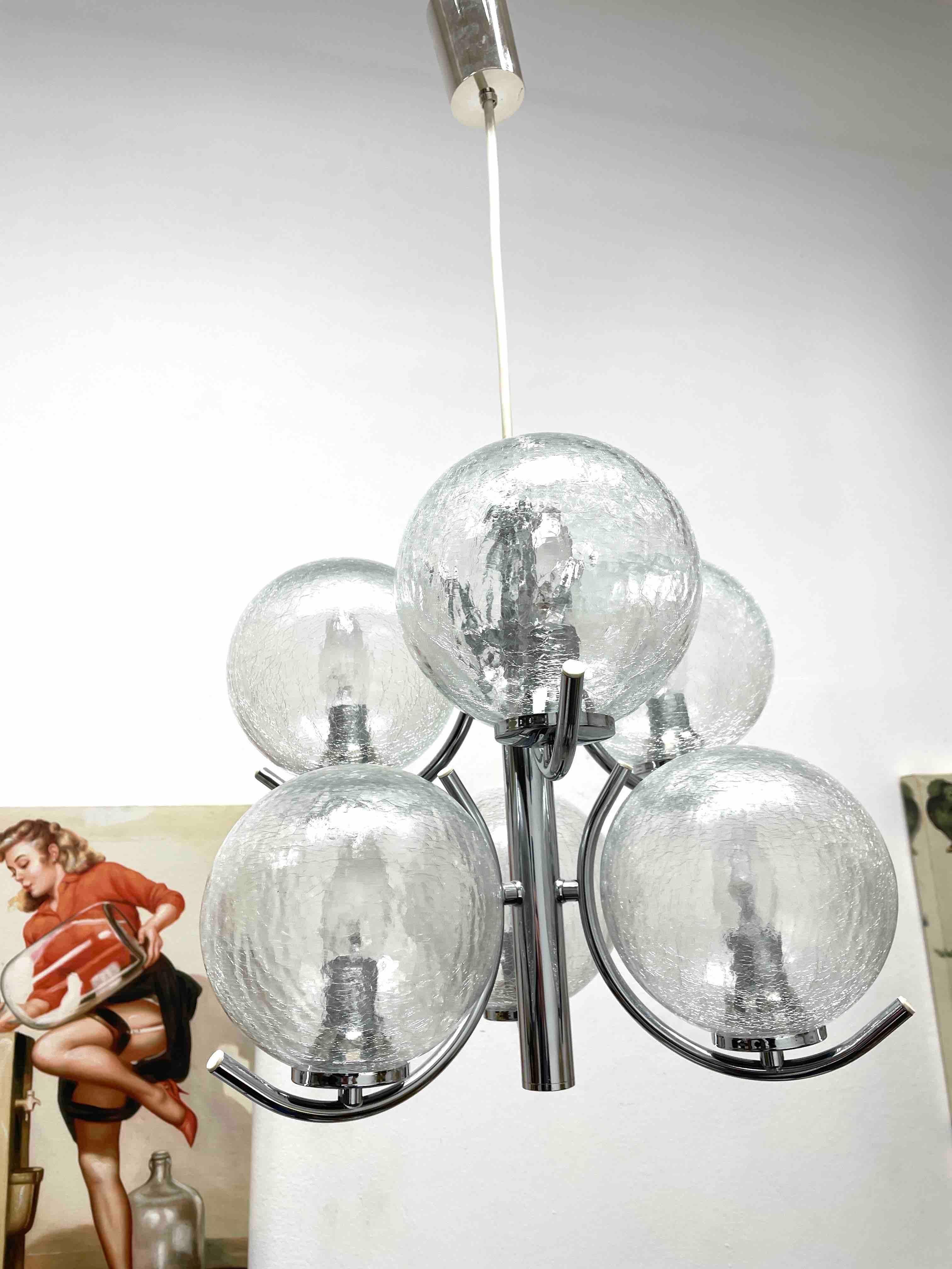 Un lustre Richard Essig fabriqué en Allemagne dans les années 1960. Il est fascinant avec son design de l'ère spatiale et ses six boules transparentes. Le corps de la lampe est entièrement en métal, y compris les bras.
Le lustre nécessite 6