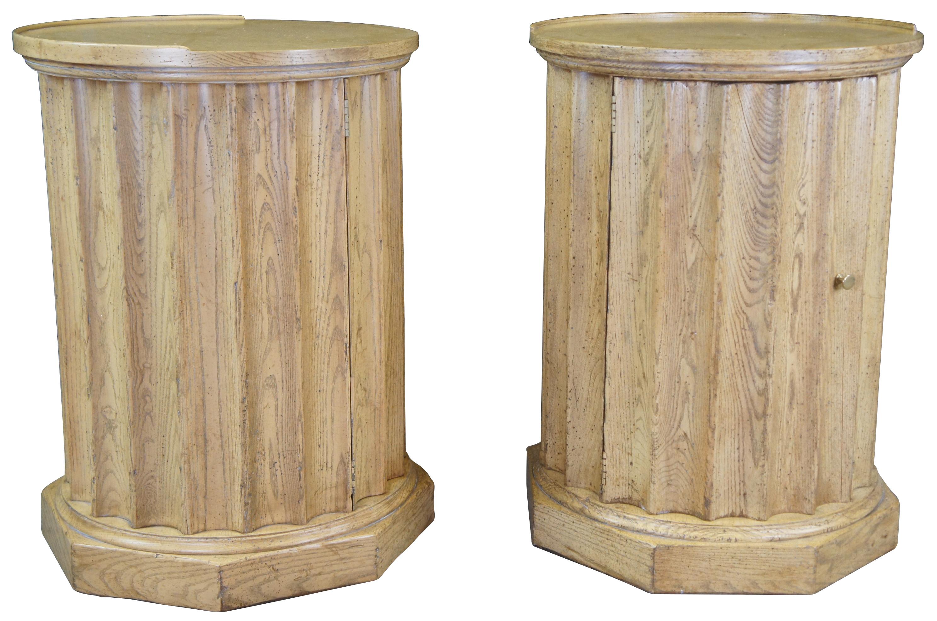 Classical pair of Baker Furniture Corinthian column style side tables, circa 1970s.  Made from oak with with a round Matchbook veneer top, scalloped center and octagonal shaped base.  Each cabinet opens to an interior shelf.  Marked  #2759 along
