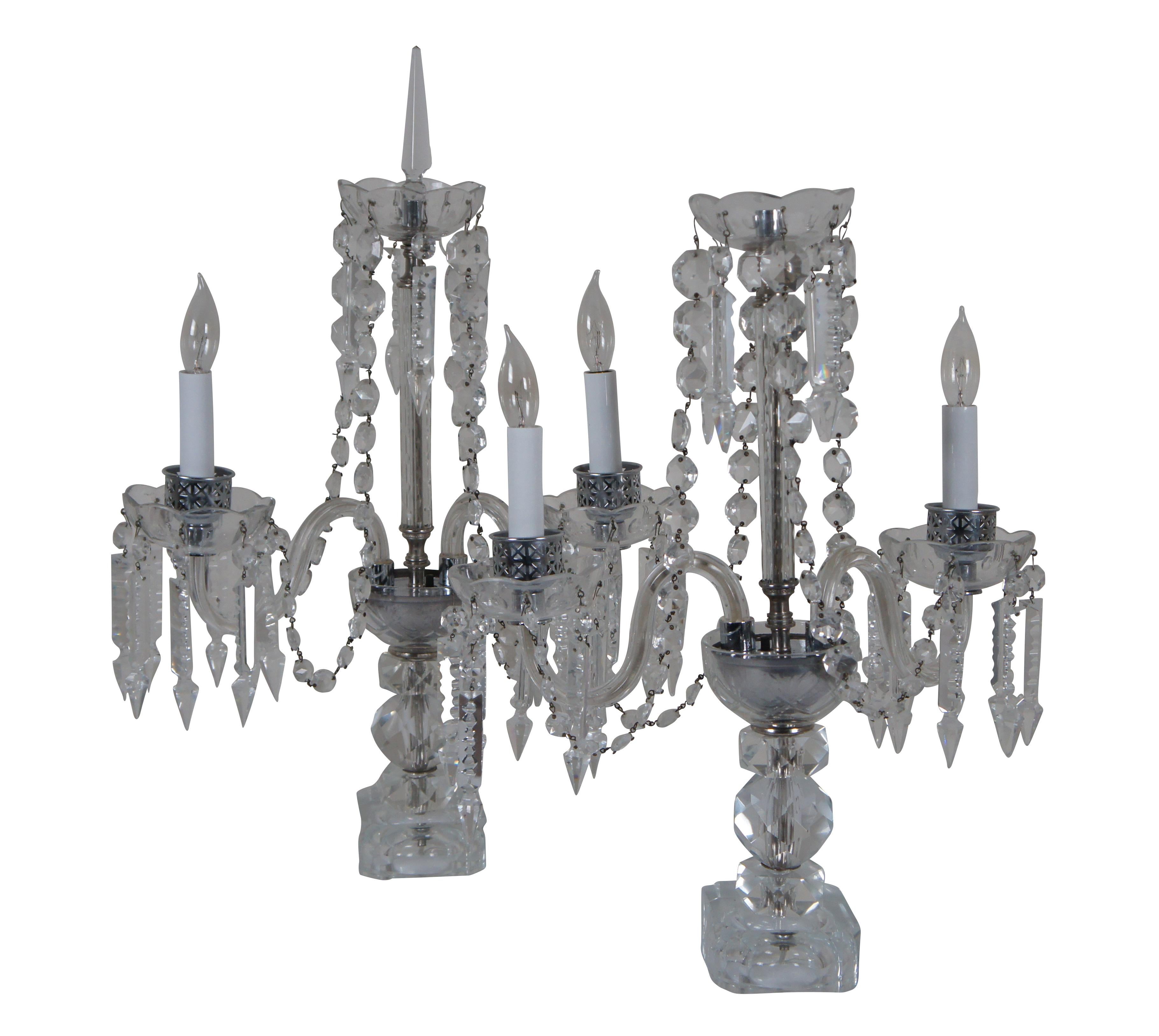 Pair of midcentury cut glass candelabra style table / buffet lamps featuring stacked faceted geometric bases supporting three candelabra arms – two illuminated and one central pillar topped with a spire finial – draped in drop crystals and beaded