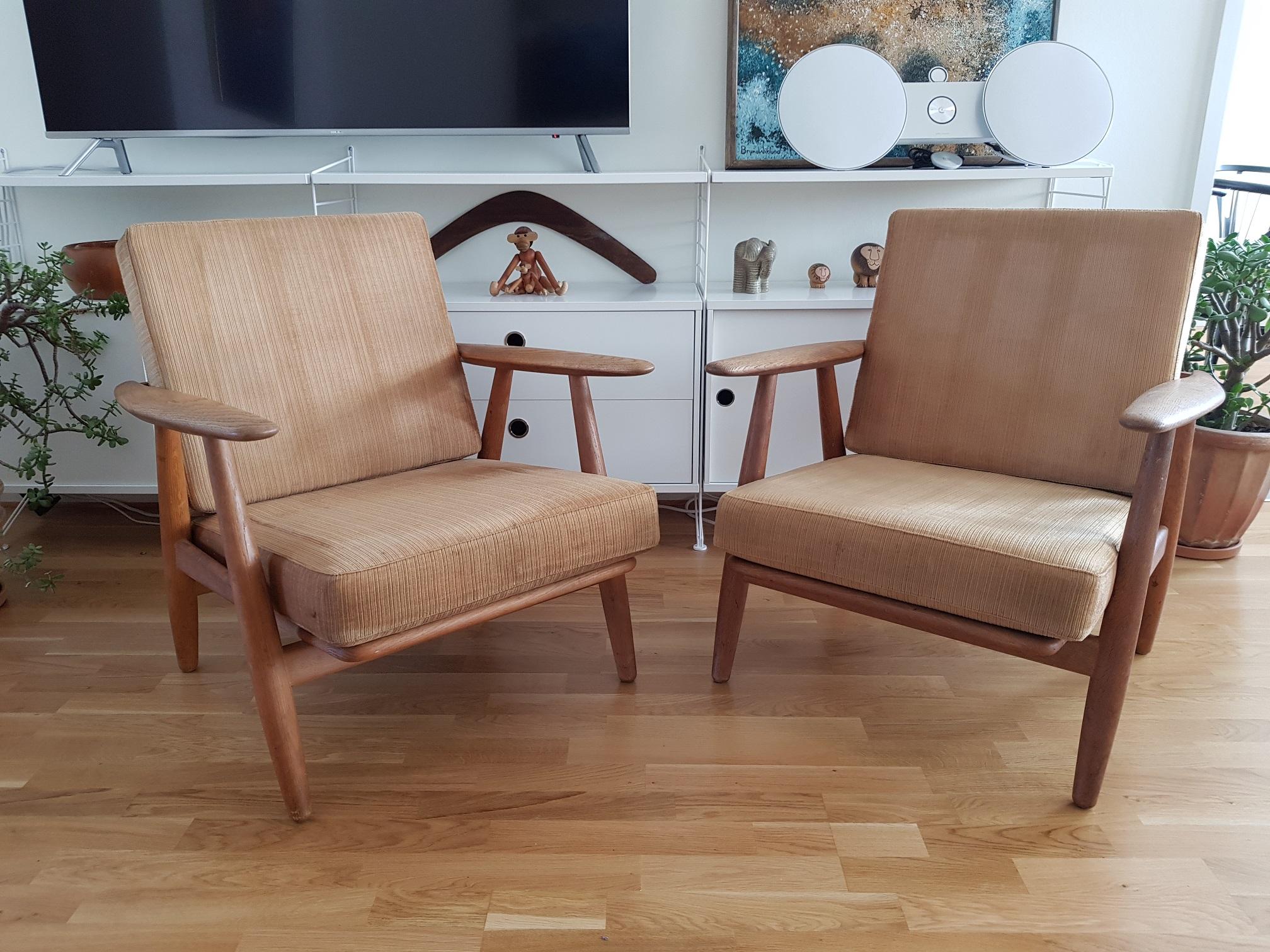 2 vintage cigar chairs made of oak with original cushions. Produced in Denmark by GETAMA in the 1960s. Design by Hans J. Wegner who is considered one of the all-time greatest mid-century Scandinavian furniture designers. These 2 lounge chairs have