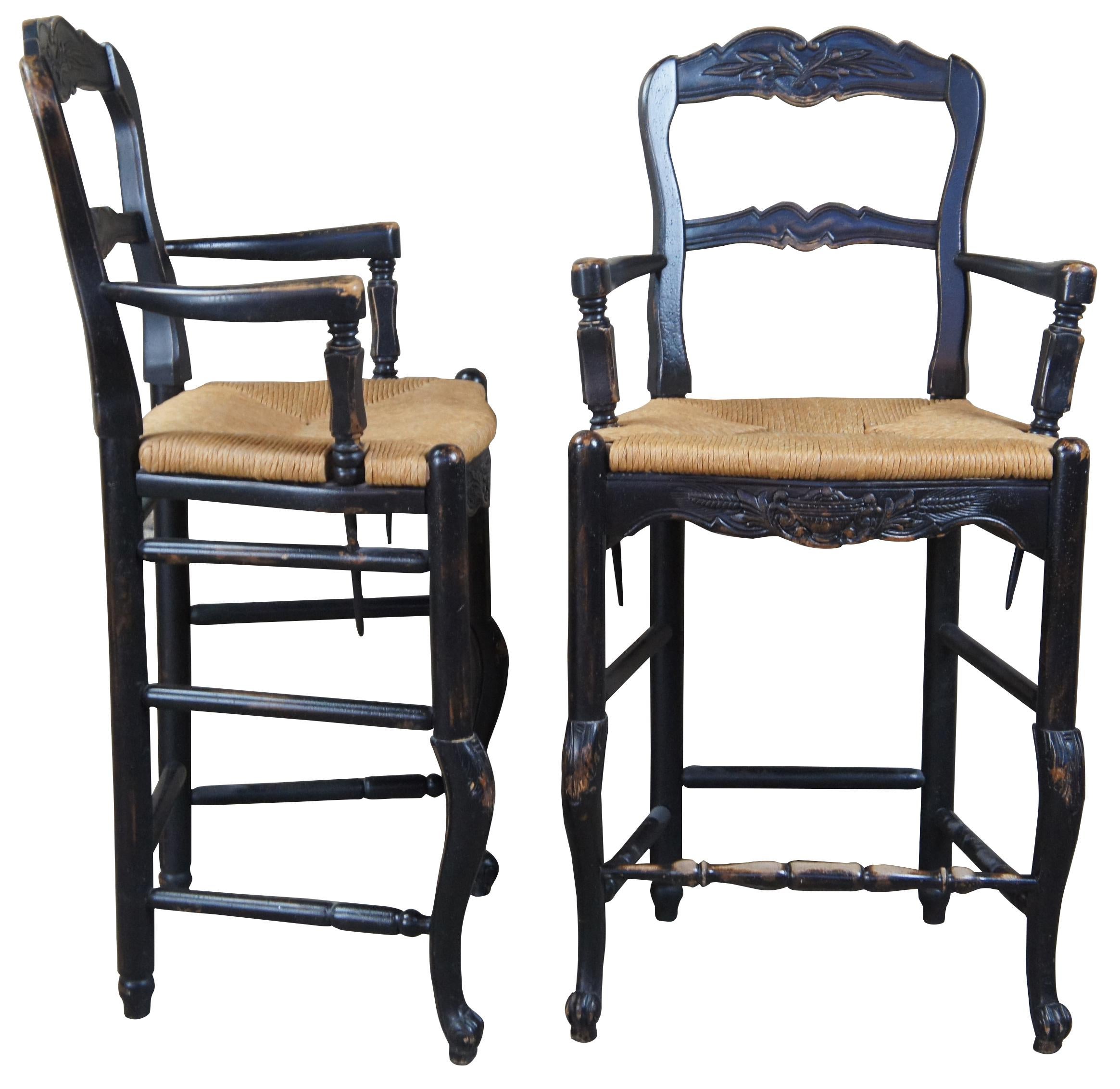 Two vintage Country French oak ladder back bar stools. Feature woven rush seats, carved floral and trophy urn elements and (Provincial inspired) cabriole legs with scrolled feet. Includes lower foot rest. Measure: 41