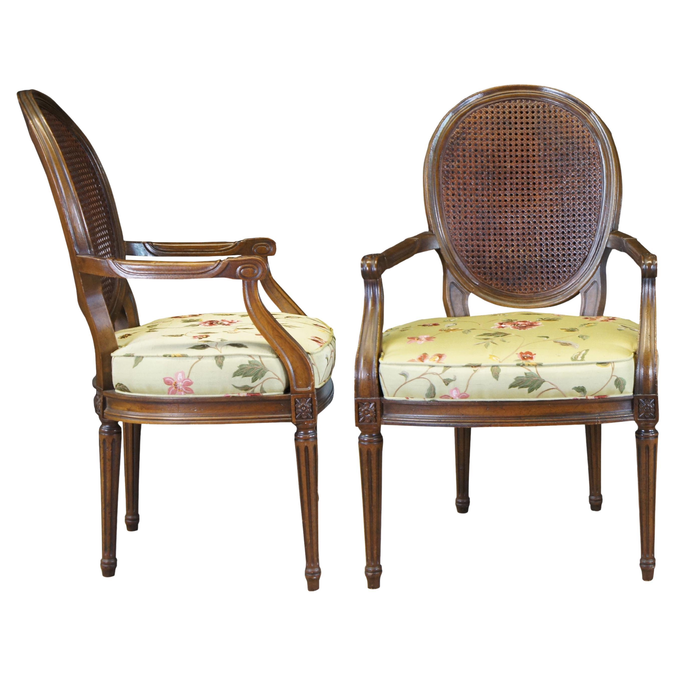 Two vintage French Louis XV armchairs. Made of walnut featuring caned oval balloon backs with a fauteuil style arm, floral / acanthus carved accents, and tapered fluted legs.
 