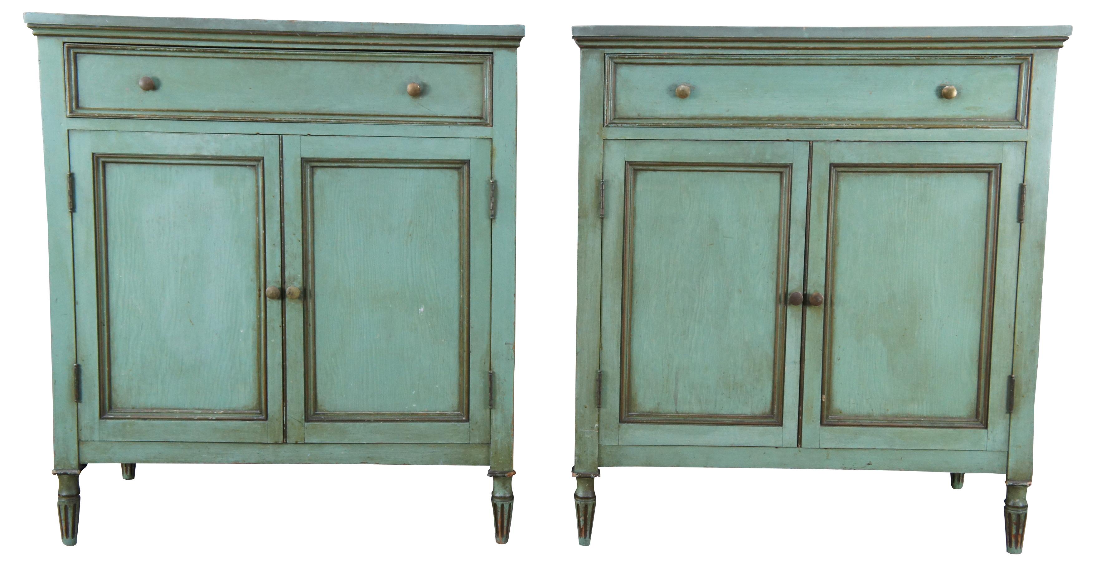 Two vintage Louis XVI style farmhouse storage cabinets. Each is in the form of an old pie safe or jelly cabinet. Featuring distressed green painted exterior with upper divided drawer and lower cabinet that opens to three pull out drawers. Suitable