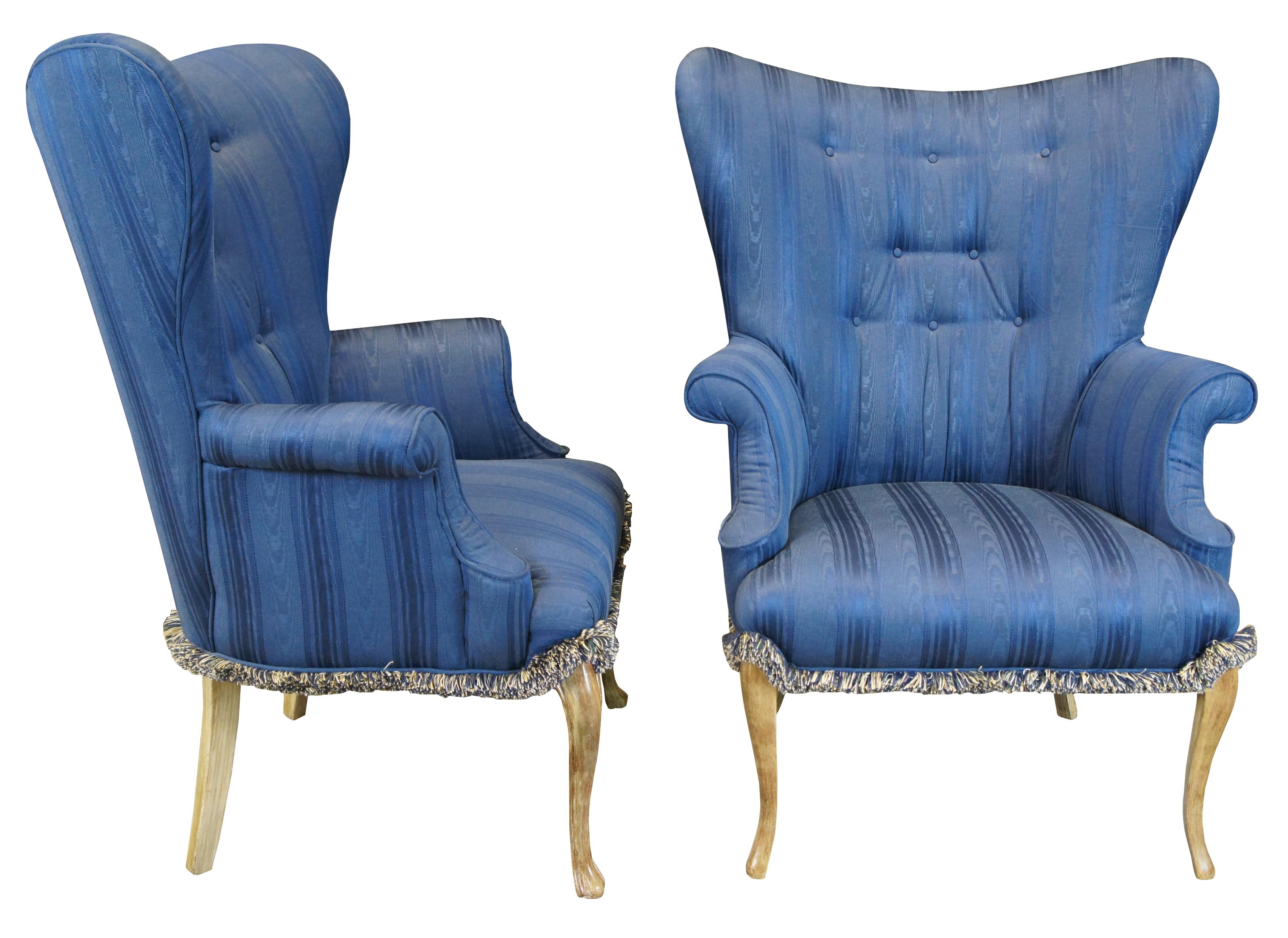 Two vintage French Provincial wingback club, library or lounge armchairs featuring serpentine form with blue striped fabric and fringe over scrolled arms, tufted flared wingback and serpentine legs. 

Measures: 32.5