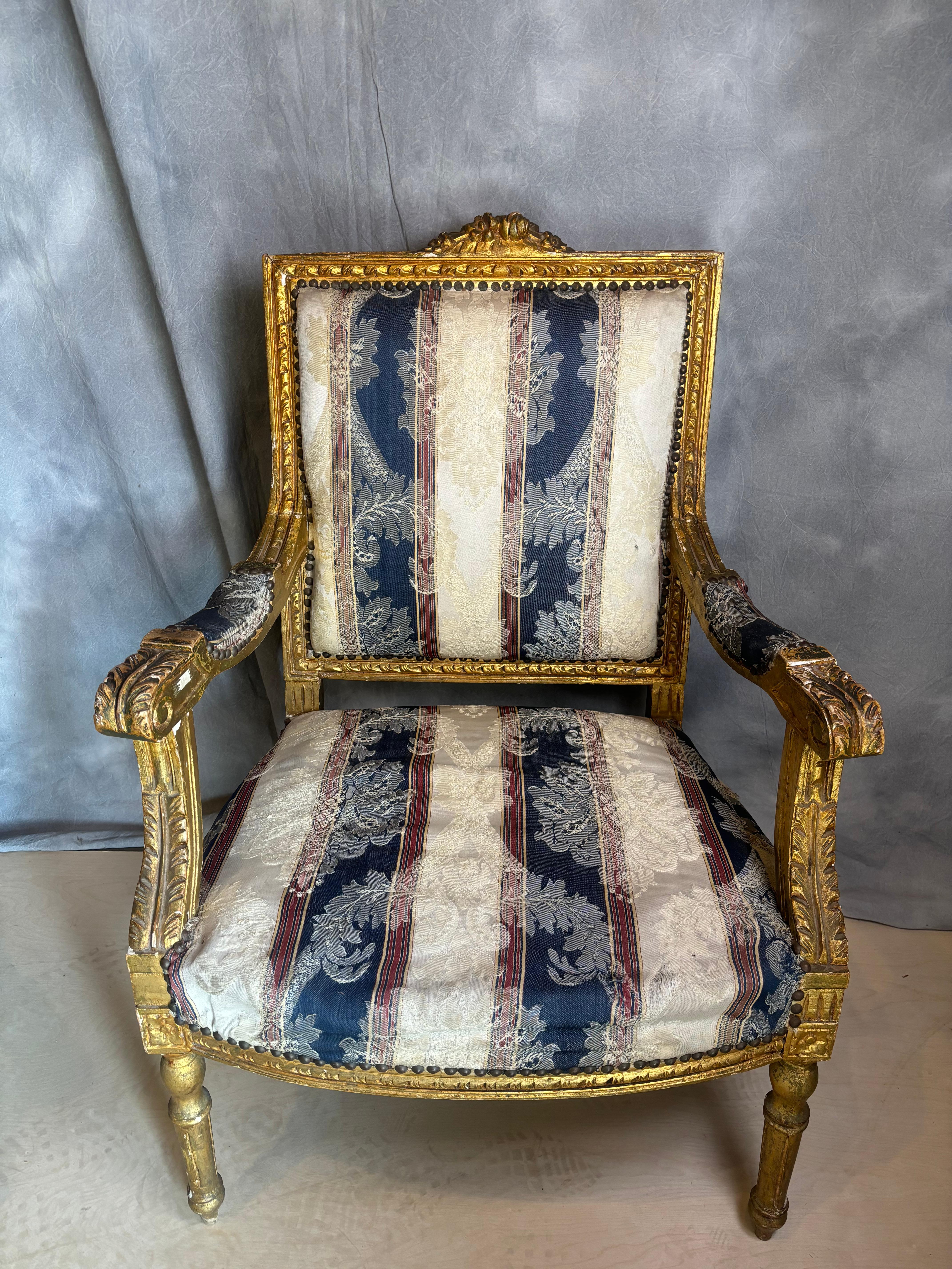 Fauteuil en bois doré sculpté de style italien, la traverse de la crête sculptée de rinceaux sur une plate-forme sculptée de rinceaux, tapissé d'un tissu rayé décoré de rinceaux et de têtes de fleurs, les accoudoirs et les supports verticaux