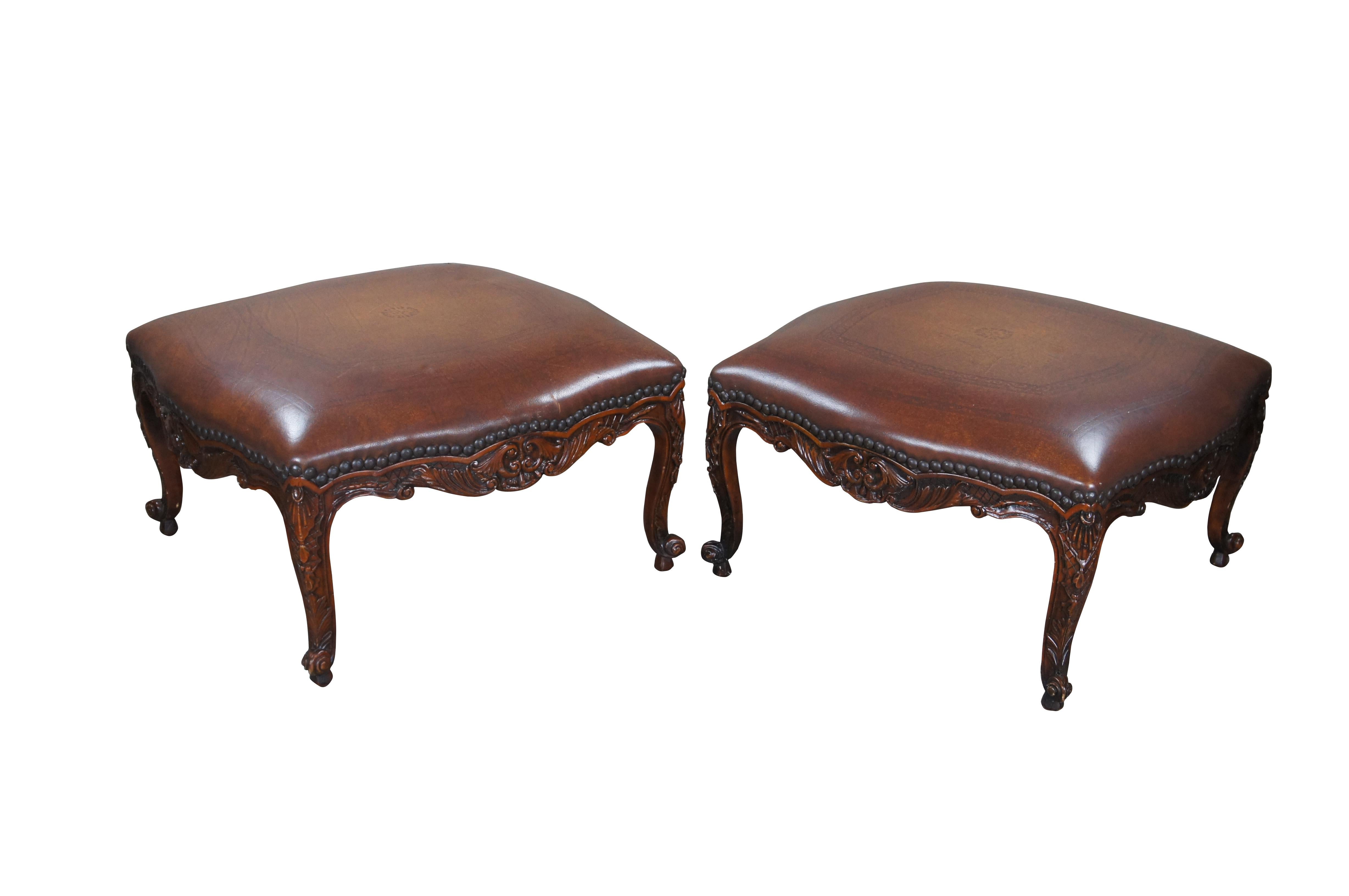 Pair of Late 20th century Ottomans / Foot stools by Theodore Alexander. French Country / Baroque inspiration with carved mahogany frames. Upholstered in brown tooled leather with nailhead trim. Includes serpentine aprons with carved lattice and