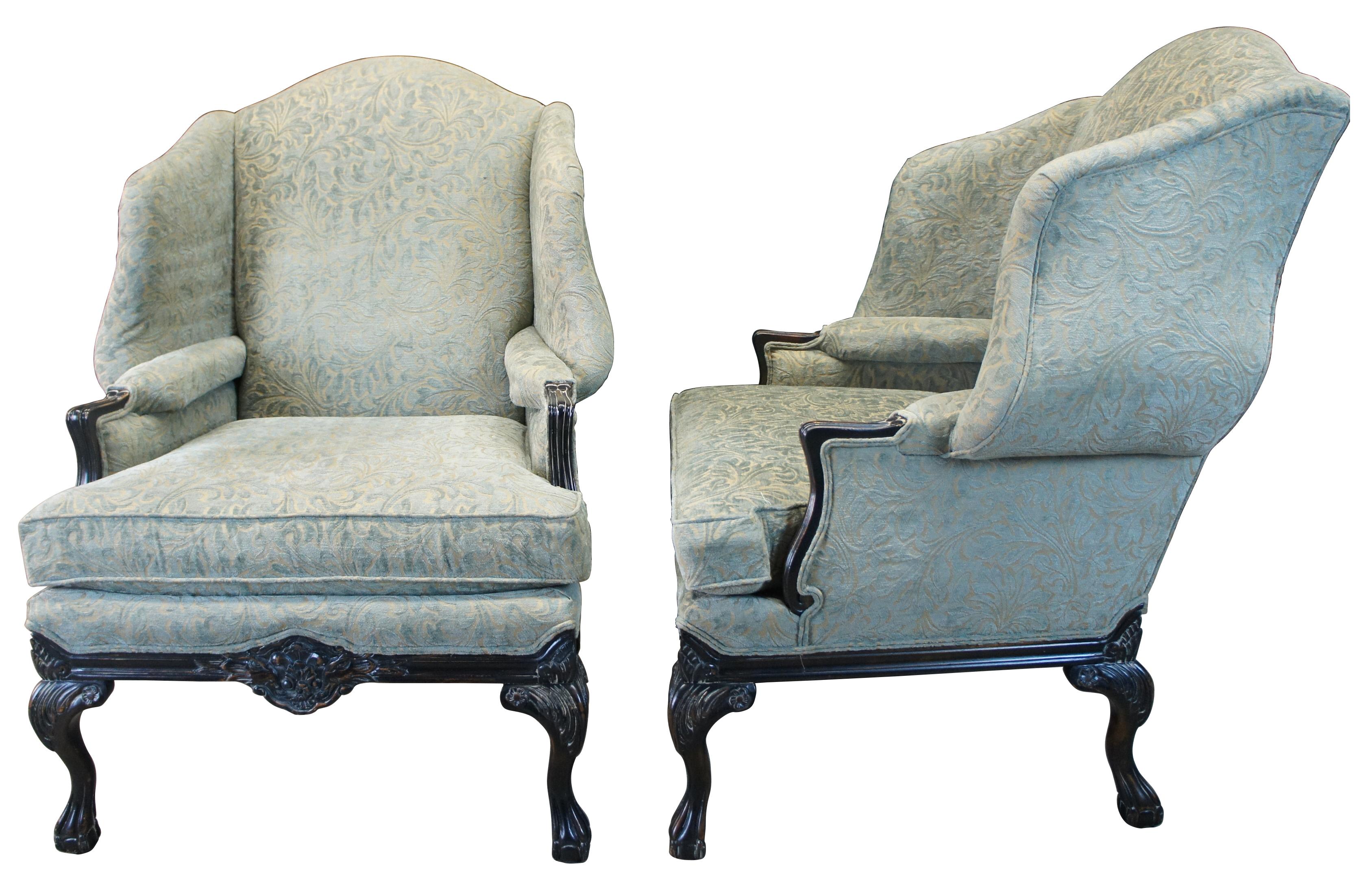 An exquisite pair of George III syle wingback chairs by Woodmark. Features a teal raised velvel floral upholstery and ebonized frame. Supported by cabriole legs leading to ball and claw feet. Includes ancathus and floral carved embellishments.