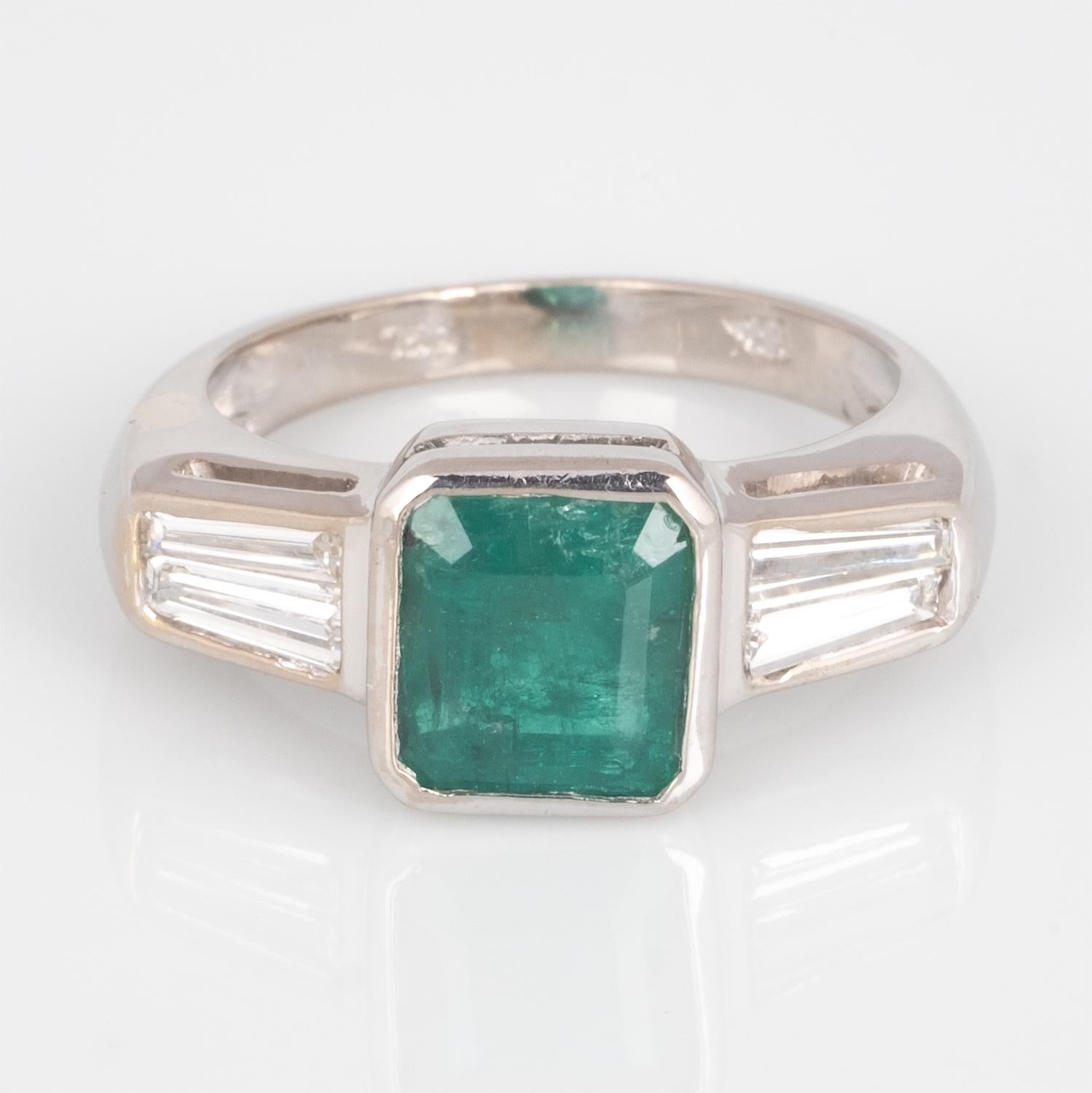 Vivid green emerald accented with 4 tapered diamond baguettes creates a sophisticated Art Deco look.
Emerald is slightly bluish green which is the most desirable color for an emerald. 
The diamond baguettes are VS clarity and G/H color. The double