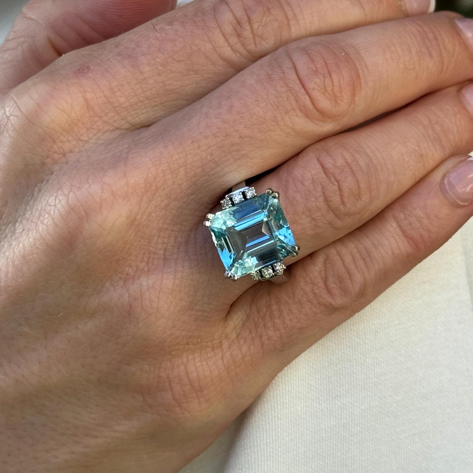 Beautiful blue aquamarine and diamond cocktail ring crafted in 14 karat white gold. The emerald cut aquamarine weighs approximately 20 carats and the 6 round brilliant cut diamond accents weigh approximately .18 carat total weight. The ring measures