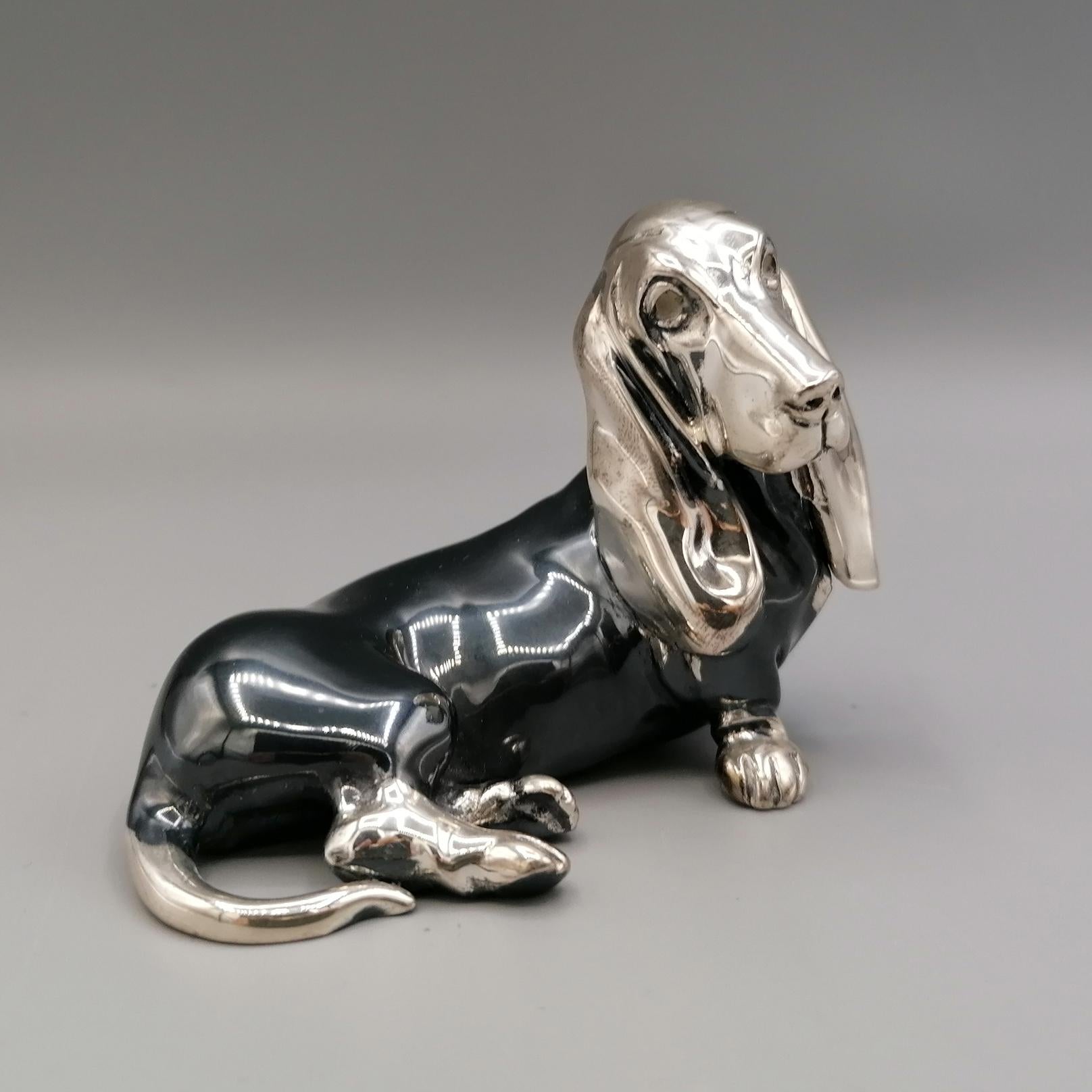 Basset Hound Hundeskulptur aus 800 massivem Silber.
Das Objekt wurde mit der Technik des Schmelzens in zwei Hälften hergestellt und anschließend durch Schweißen verbunden. 
Im unteren Teil der Statuette sind die beiden Löcher zu sehen, durch die
