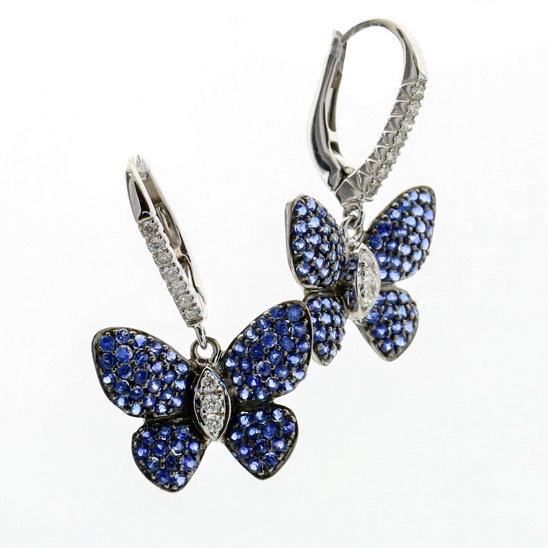 Dangle butterfly earrings in 18-karat white gold with sapphires and diamonds. The butterflies dangle from a polished metal lever-back with diamond accents. Butterfly wings are pave-set with round-cut natural blue sapphires, and the body has 3