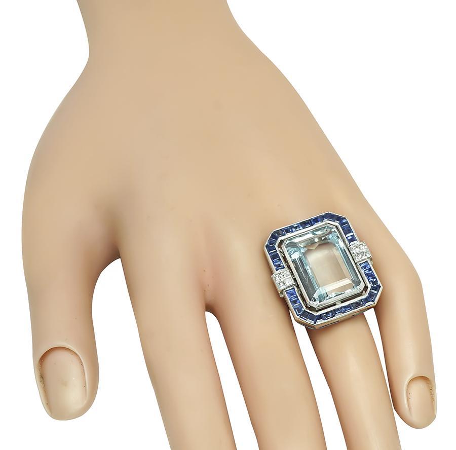 Dies ist ein erstaunlicher Platinring. In der Mitte des Rings befindet sich ein schöner Aquamarin im Smaragdschliff mit einem Gewicht von ca. 20,00ct. Der Mittelstein wird von quadratisch geschliffenen Saphiren und Diamanten im Prinzessschliff mit