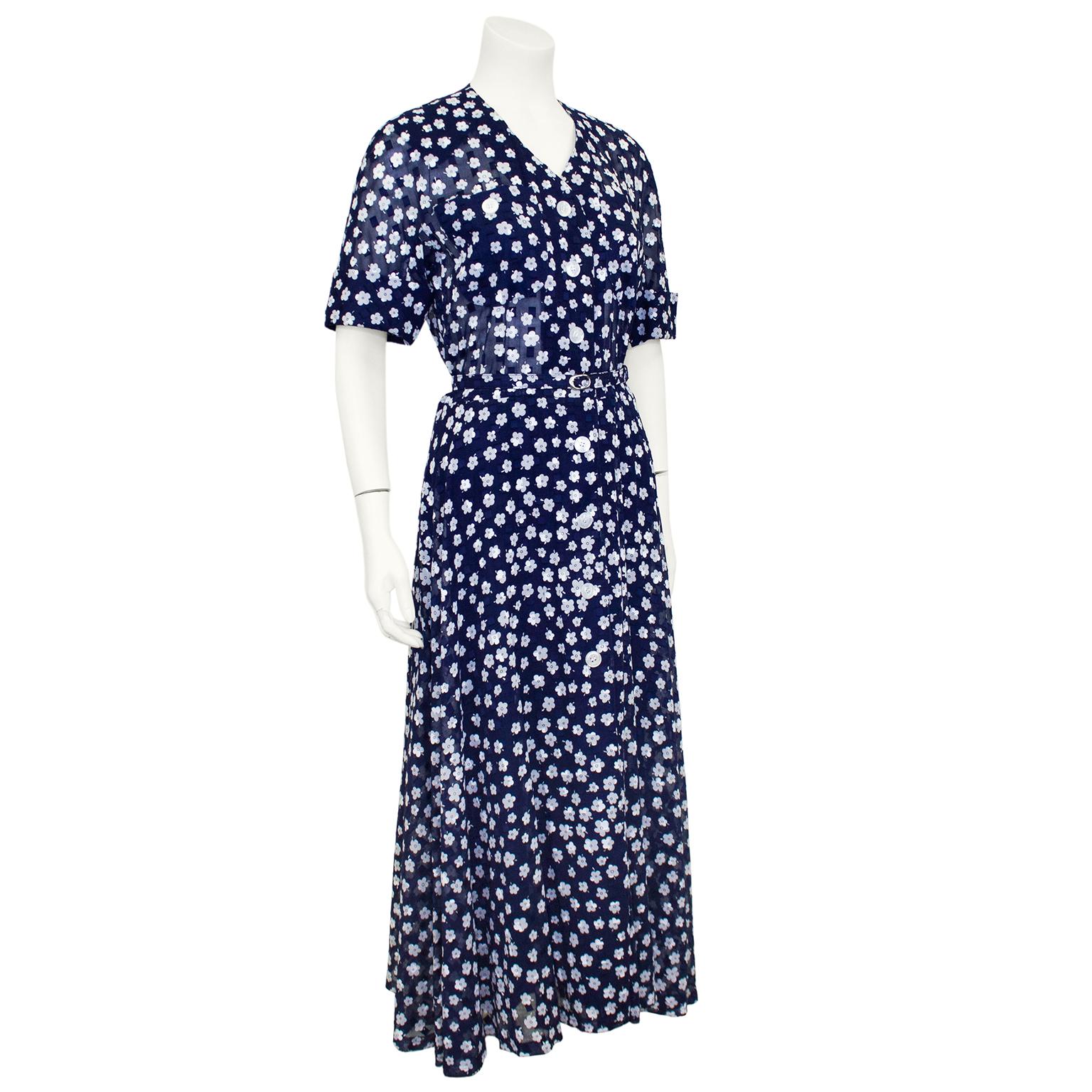 Beautiful and elegant Akris shirt dress from the 2000's. Navy blue cotton jacquard with all over monochromatic squares and white flowers. V neckline, cuffed short sleeves and belted at the waist. Patch pockets at bust and large, round white plastic