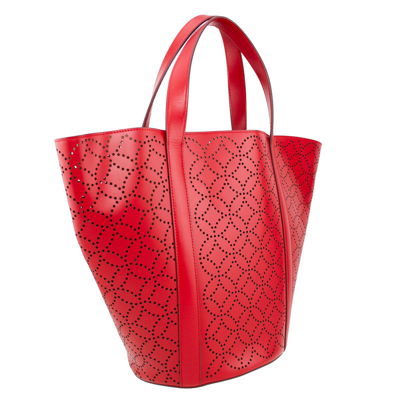 Beautiful, luxurious and unused Alaia bag. Laser cut supple red leather in an iconic Alaia pattern. Open top and flat top handles with tonal top stitching. Interior red leather wristlet with silver top zipper and beige interior. Wristlet has a