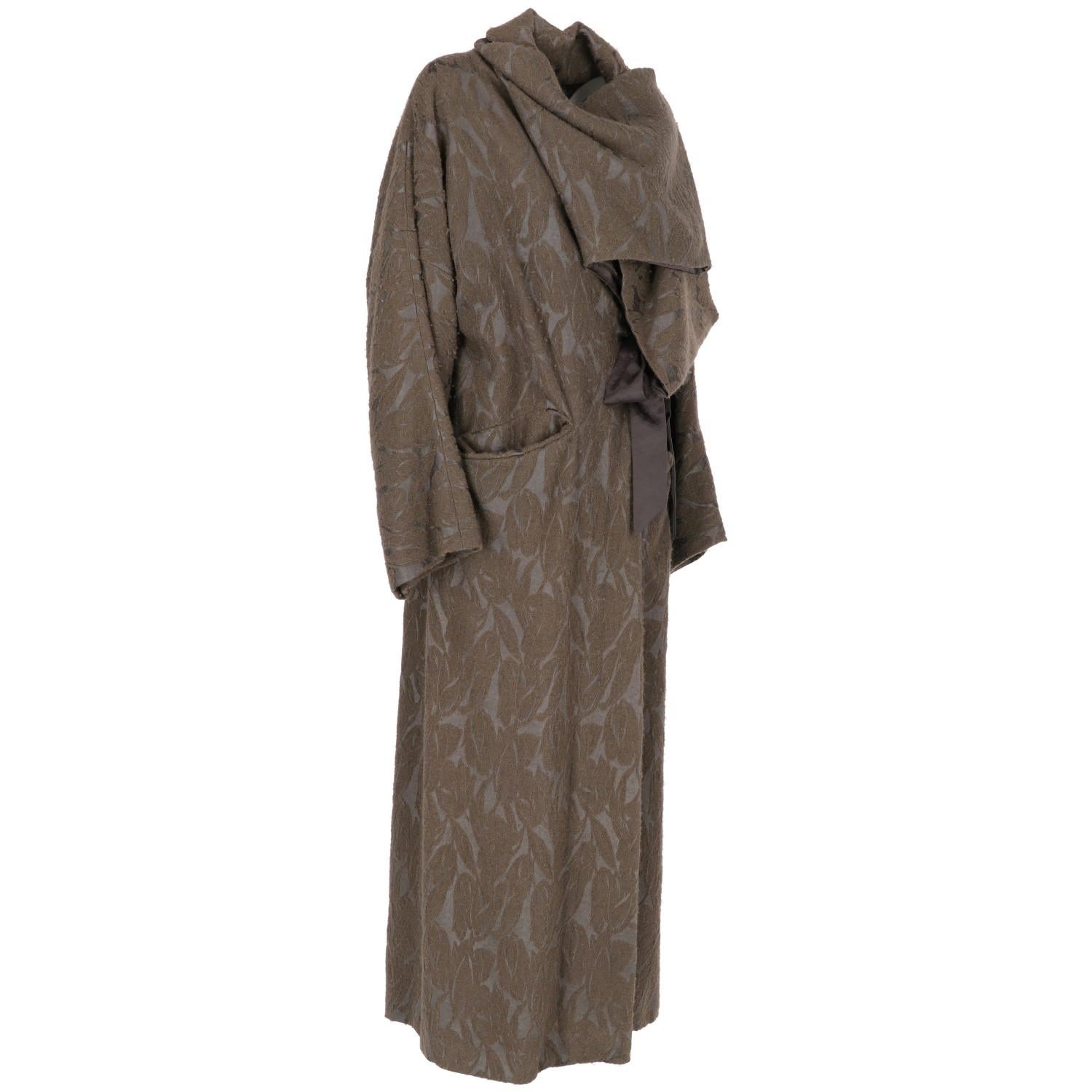 The Antonio Marras long brown jacquard wool coat with grey satin inner inserts features one wrap collar, waistband and single-buttoned front closure and two fancy cut front pockets. The lining is in grey flower and stripes pattern jacquard satin.