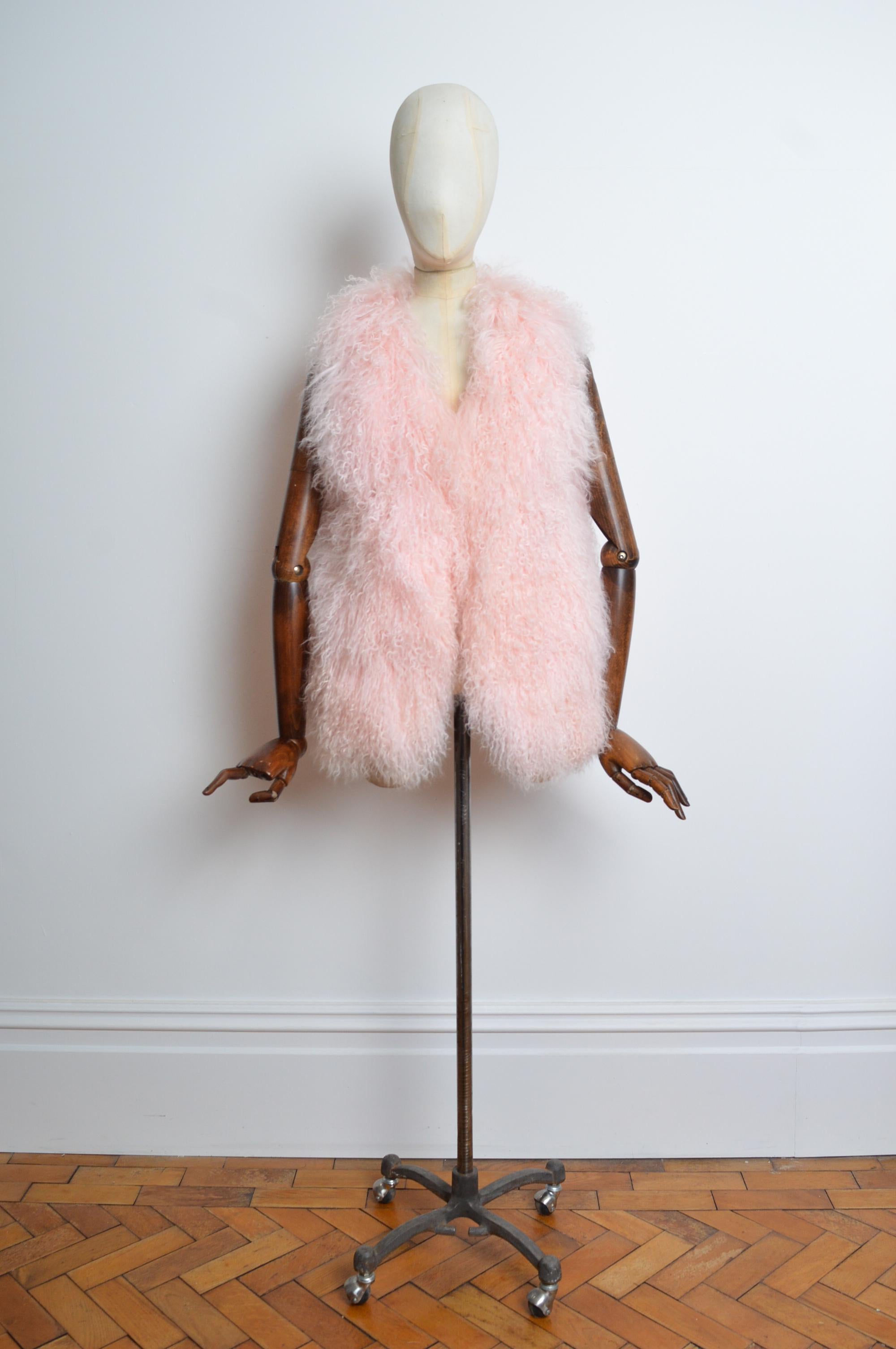Fabulous 2000's soft & shaggy baby pink Mongolian Lamb gilet. Crafted from thick & curly pelts, featuring pockets at the hips and fully lined interior, farrier hook fasten closure.
Size; One Size. Small fit / UK 6 - 8. 
Measurements are provided in