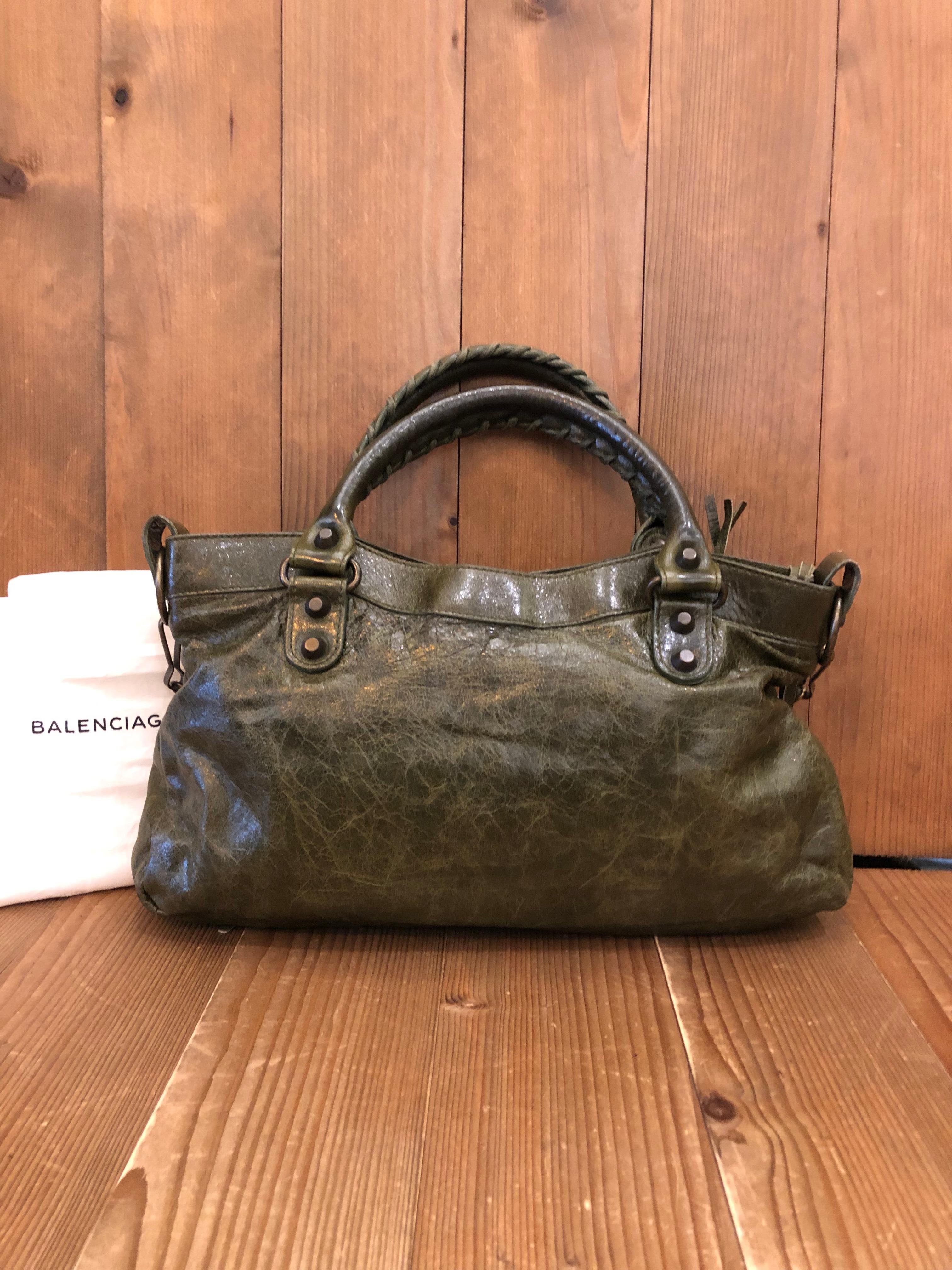 This Balenciaga First bag is Crafted of khaki distressed lambskin leather featuring hand stitched handles and a removable shoulder strap of the same leather and a zip pocket at the front. Zipper top closure. Interior is lined with fabric and has one