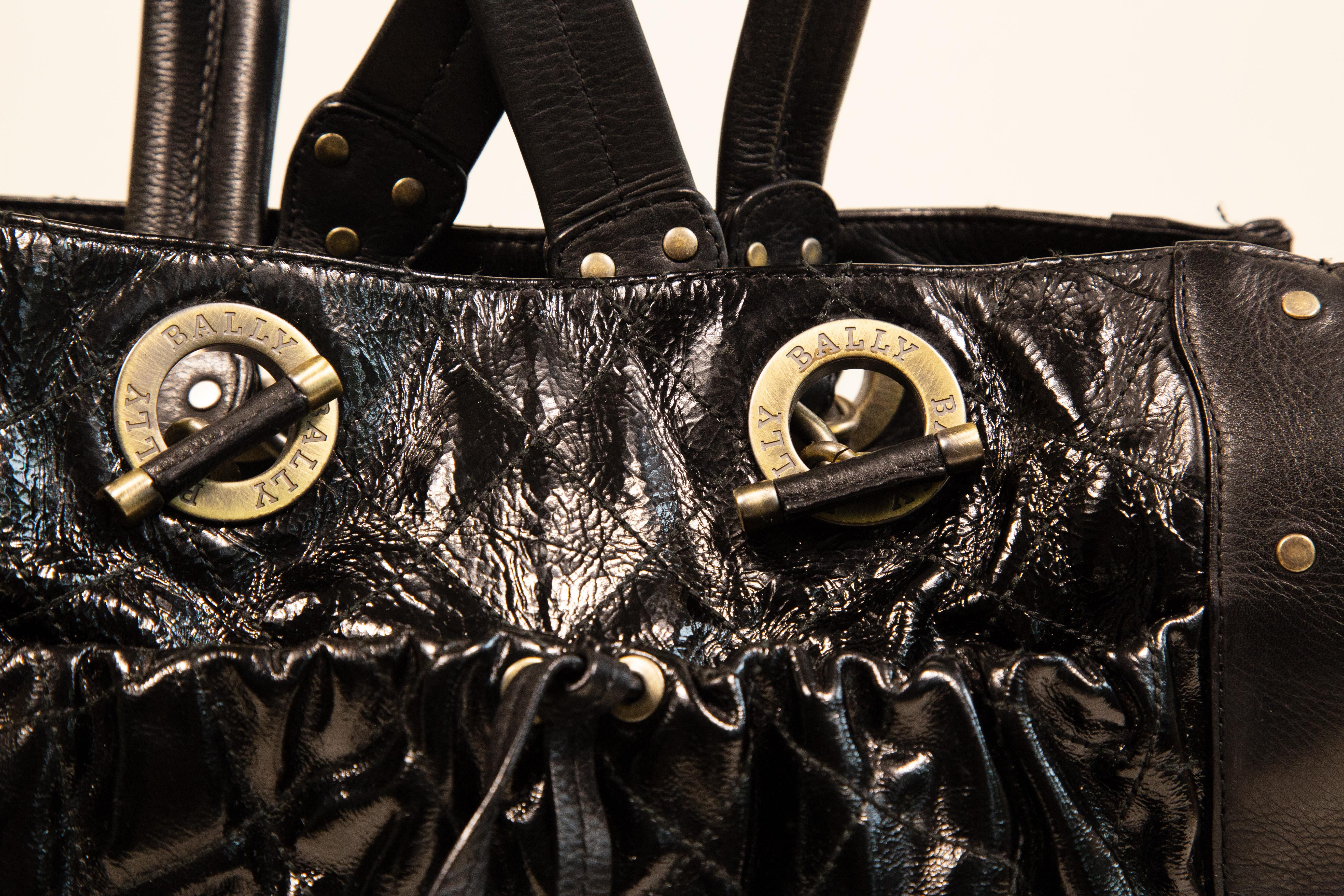 Bally Umhängetasche aus schwarzem Lackleder mit schwarzer Glattlederoberfläche und altmessingfarbener Hardware. Die  Das Innere ist mit Stoff ausgekleidet und hat neben dem Hauptfach eine Seitentasche mit Reißverschluss. Darüber hinaus gibt es eine