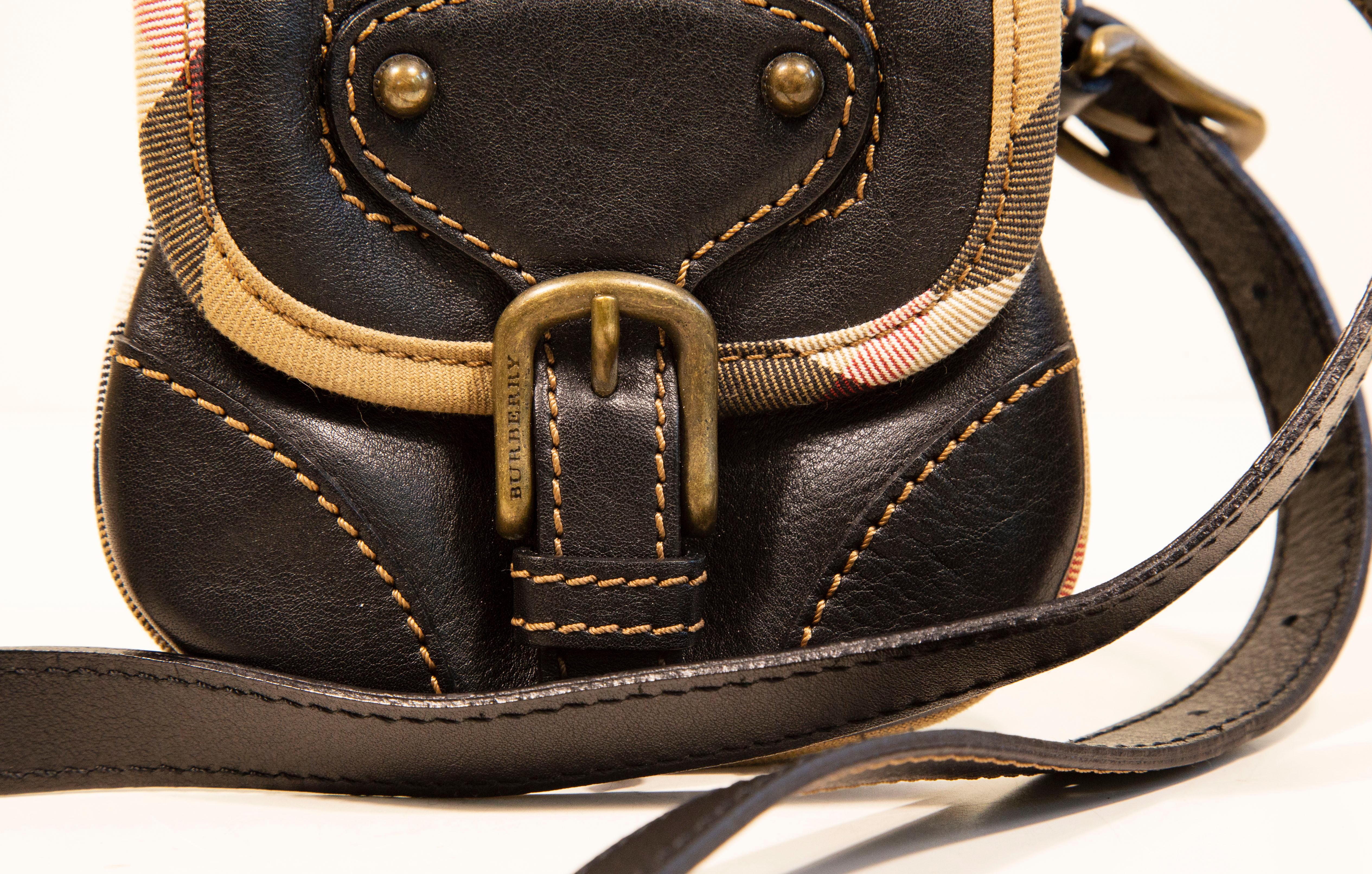 Minibolso Burberry de piel marrón con herrajes en tono bronce viejo. El bolso está acabado con un ribete de lona con el estampado de cuadros Burberry. El interior está forrado de lona negra y consta de un compartimento. La correa para el hombro es