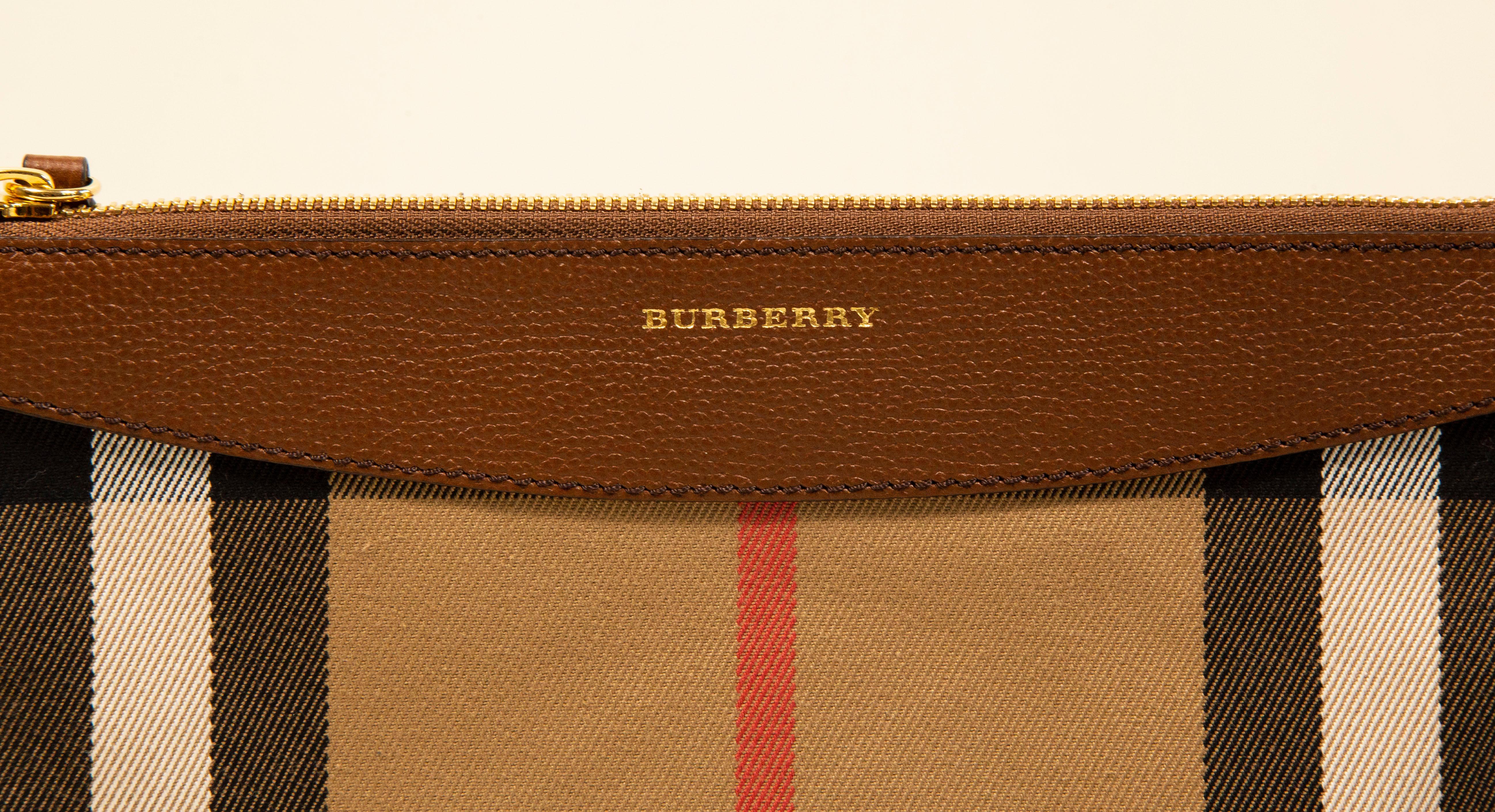 Burberry clutch/crossbody bag made of the Burberry check canvas with brown leather trim and gold toned hardware. The interior is lined with synthetic fabric and next to the major compartment it features four slots for cards. The shoulder strap is