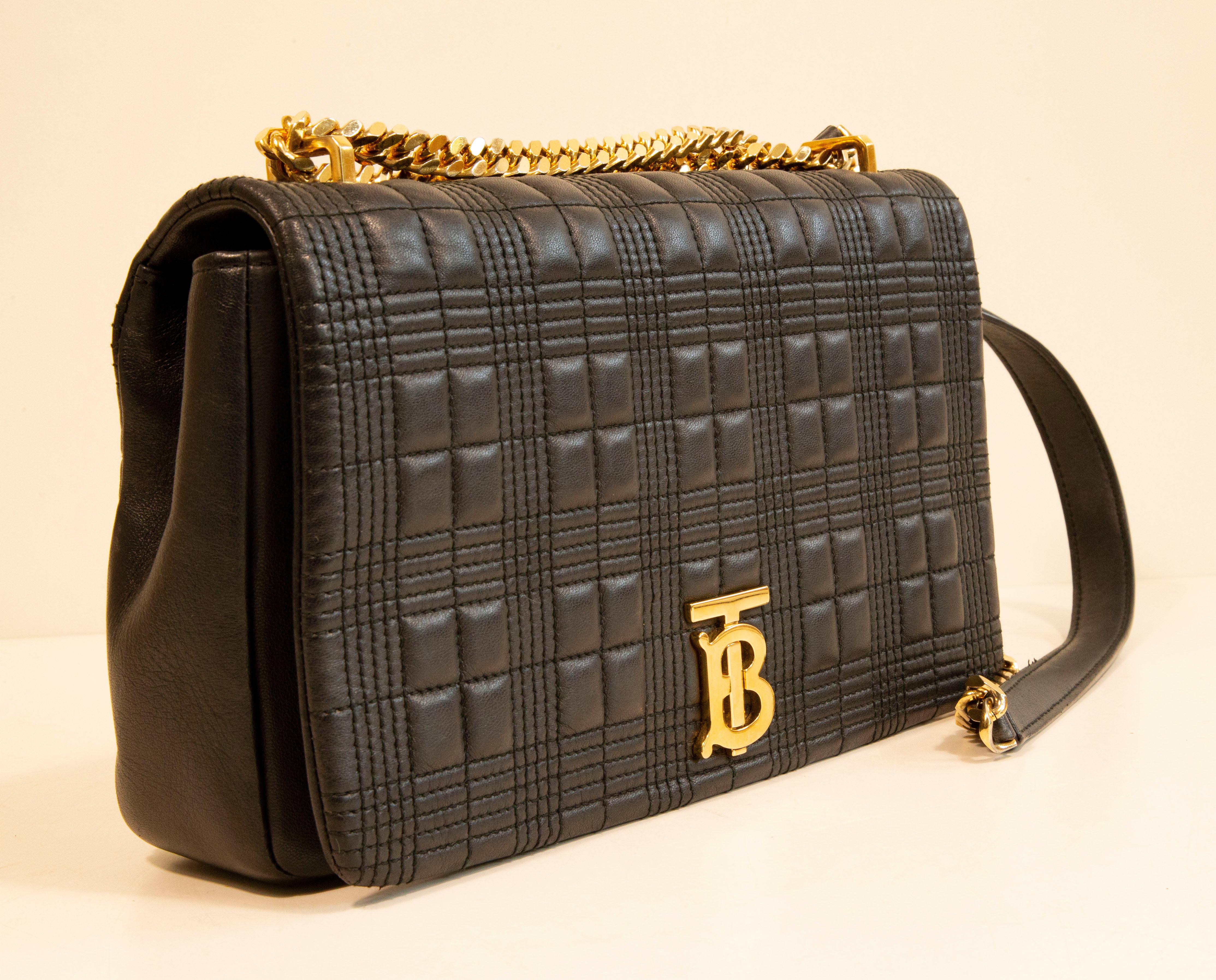 A Burberry medium Lola bag made of black quilted leather with gold toned hardware. The interior is lined with black fabric and next to the major compartment it features, one side pocket with a zipper. The bag can be worn as a cross body bag or as a