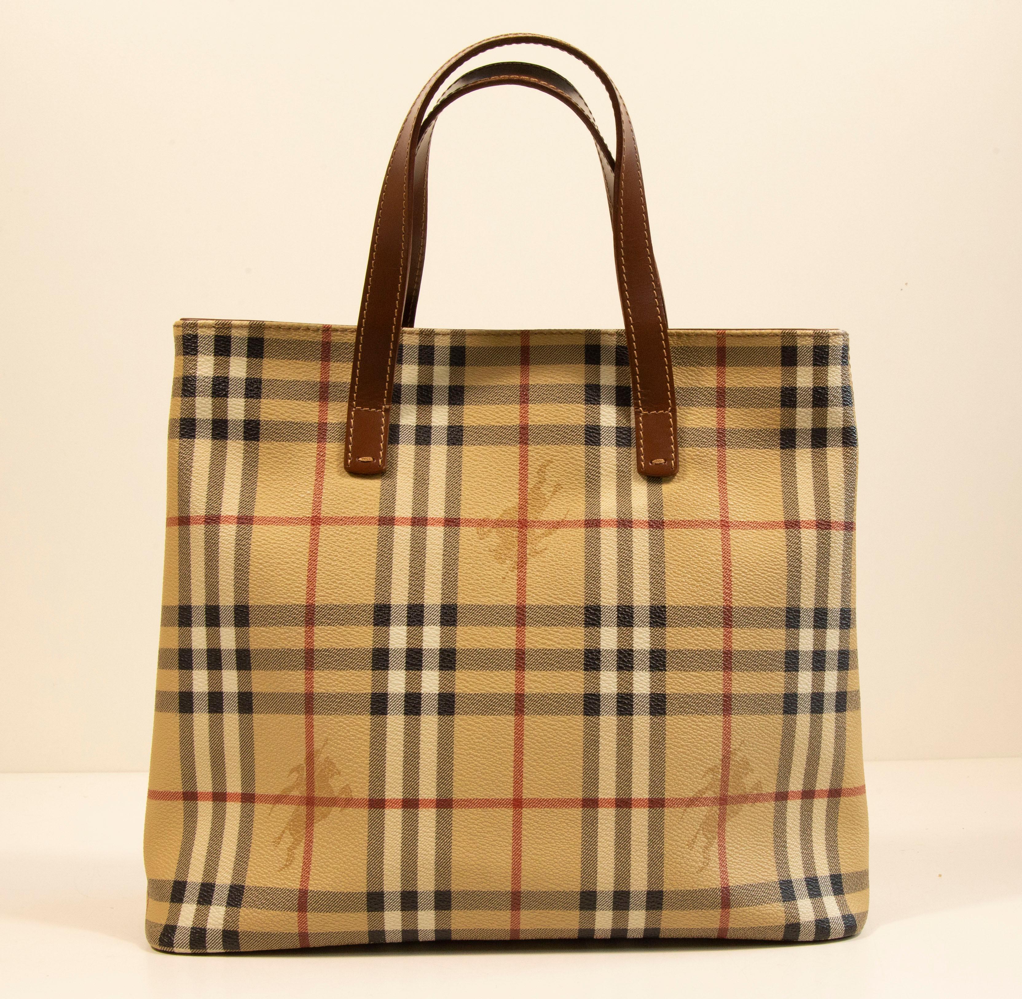 Un sac à main/shopper Burberry en toile enduite de vinyle avec les carreaux classiques Burberry et une finition en cuir marron. L'intérieur est doublé de tissu noir et comporte, à côté du compartiment principal, une poche latérale à fermeture