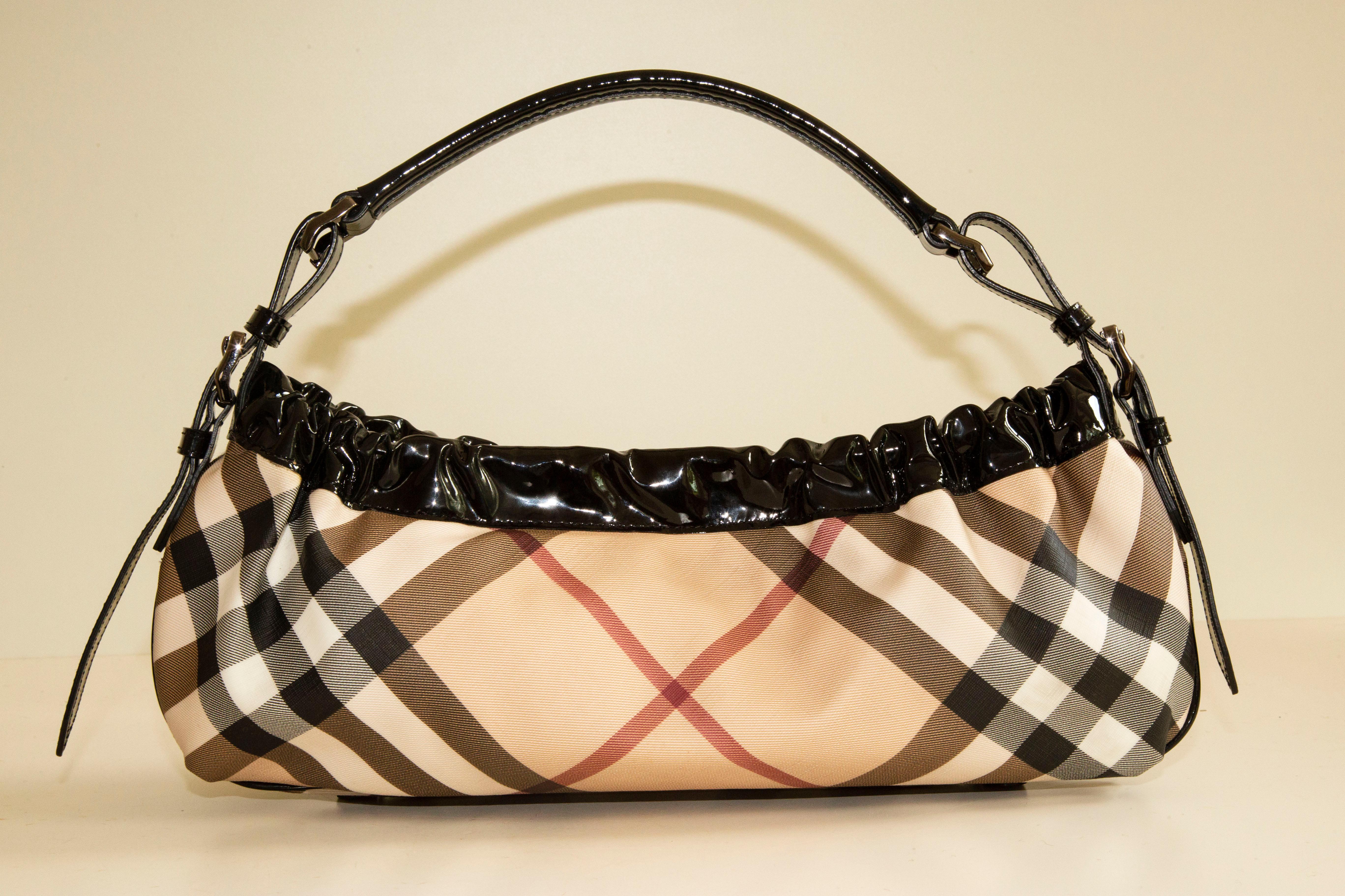 A Burberry shoulder bag made of coated canvas with the Nova Check pattern.
The bag is finished with black patent leather trim and pewter toned hardware.
The interior is lined with beige fabric. It consists of two major compartments. In addition, it