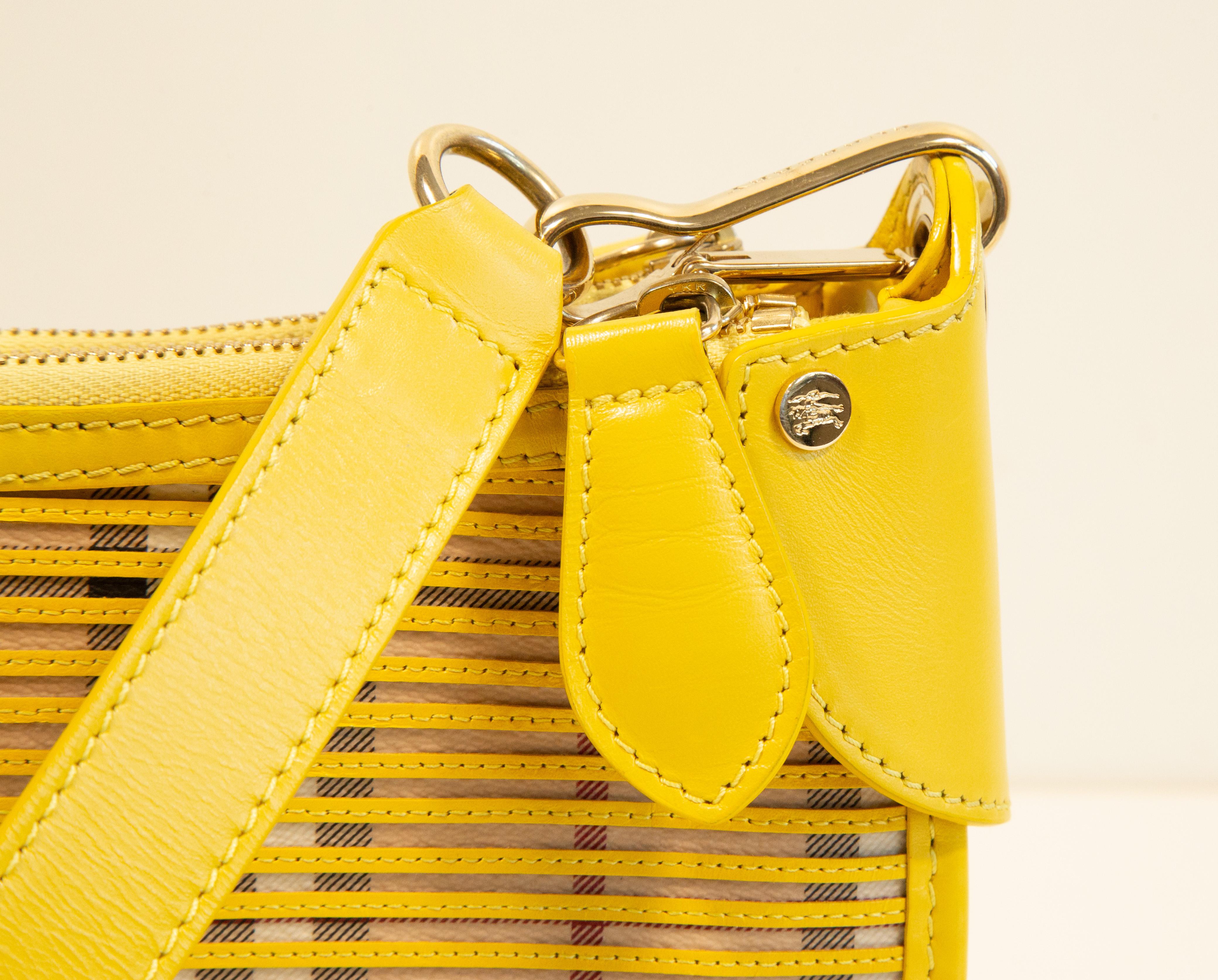 A Burberry shoulder bag/clutch made of vinyl coated canvas with the classic Burberry check, covered with yellow leather trim. The bag features gold toned hardware. The shoulder strap is 54 cm long, 24 cm drop, and it can be detached from the bag.