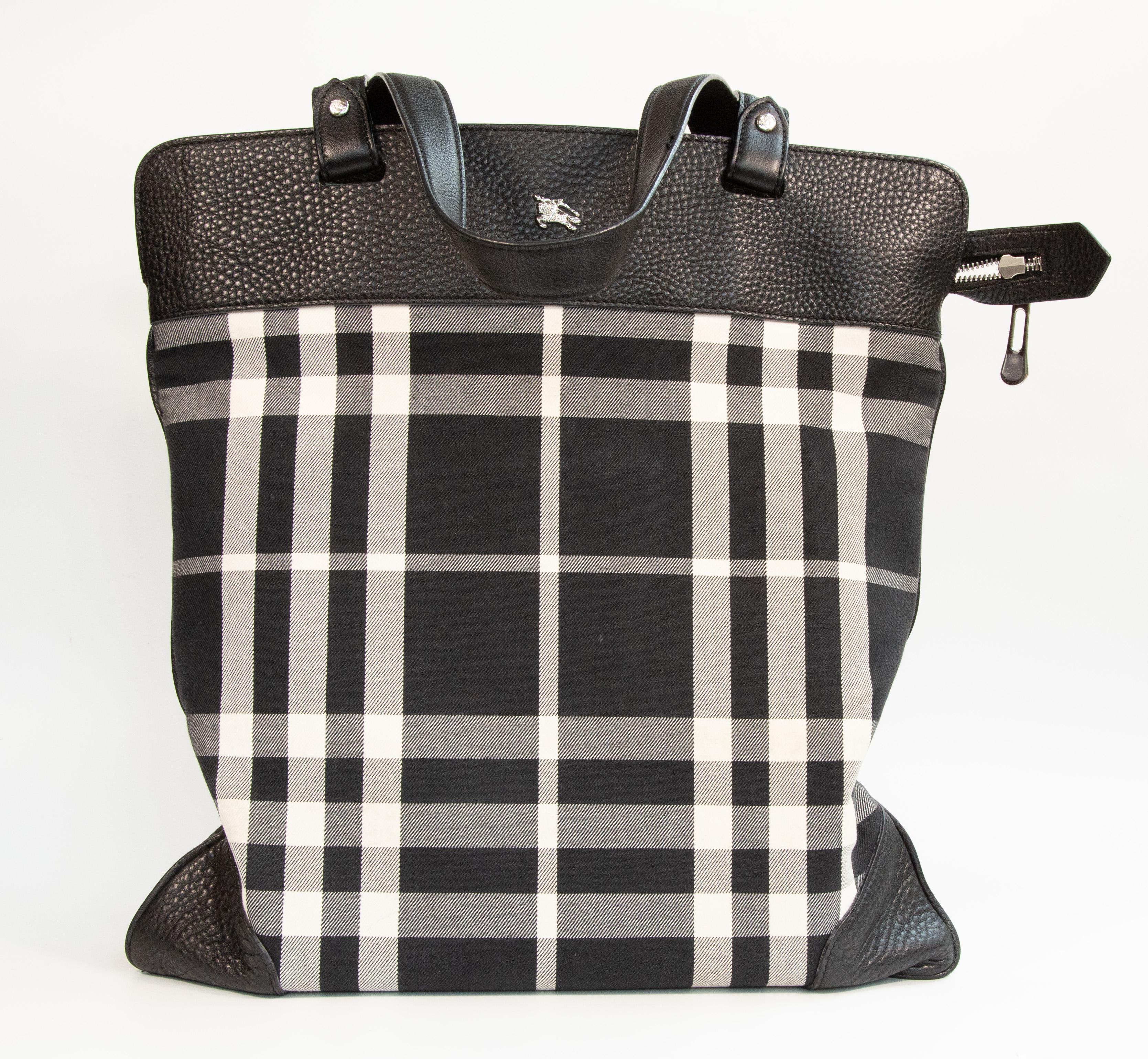 A Burberry tote/shoulder bag made of black & white canvas with the Burberry tartan pattern. The bag features black leather trim and silver toned hardware. The interior is lined with a purple canvas  and next to the major compartment it features