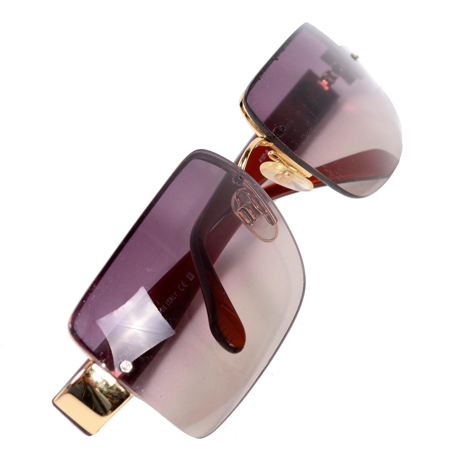 These Chanel sunglasses are from the early 2000's. They have the look of rimless from the front, with rectangular shape and gold accents. The glass is a purple gradient and the arms are sheer brown plastic with gold interlocking CC logos. The gold