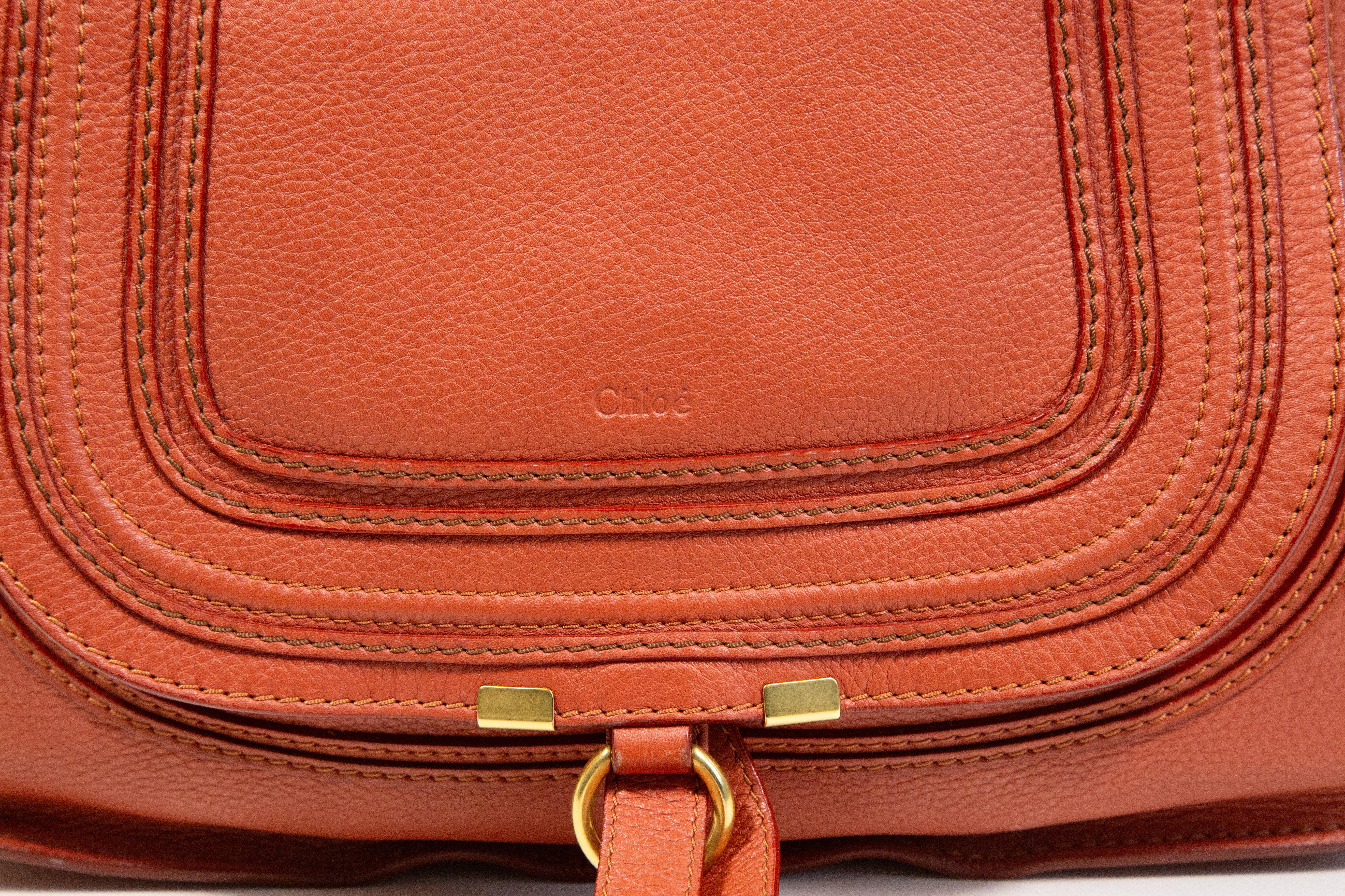 Chloe Marcie shoulder bag/top handle bag made of leather in red/orange. The hardware is gold toned. The interior is lined with fabric and next to the major compartment it features two side pockets of which one has a zipper. The bag has minor signs